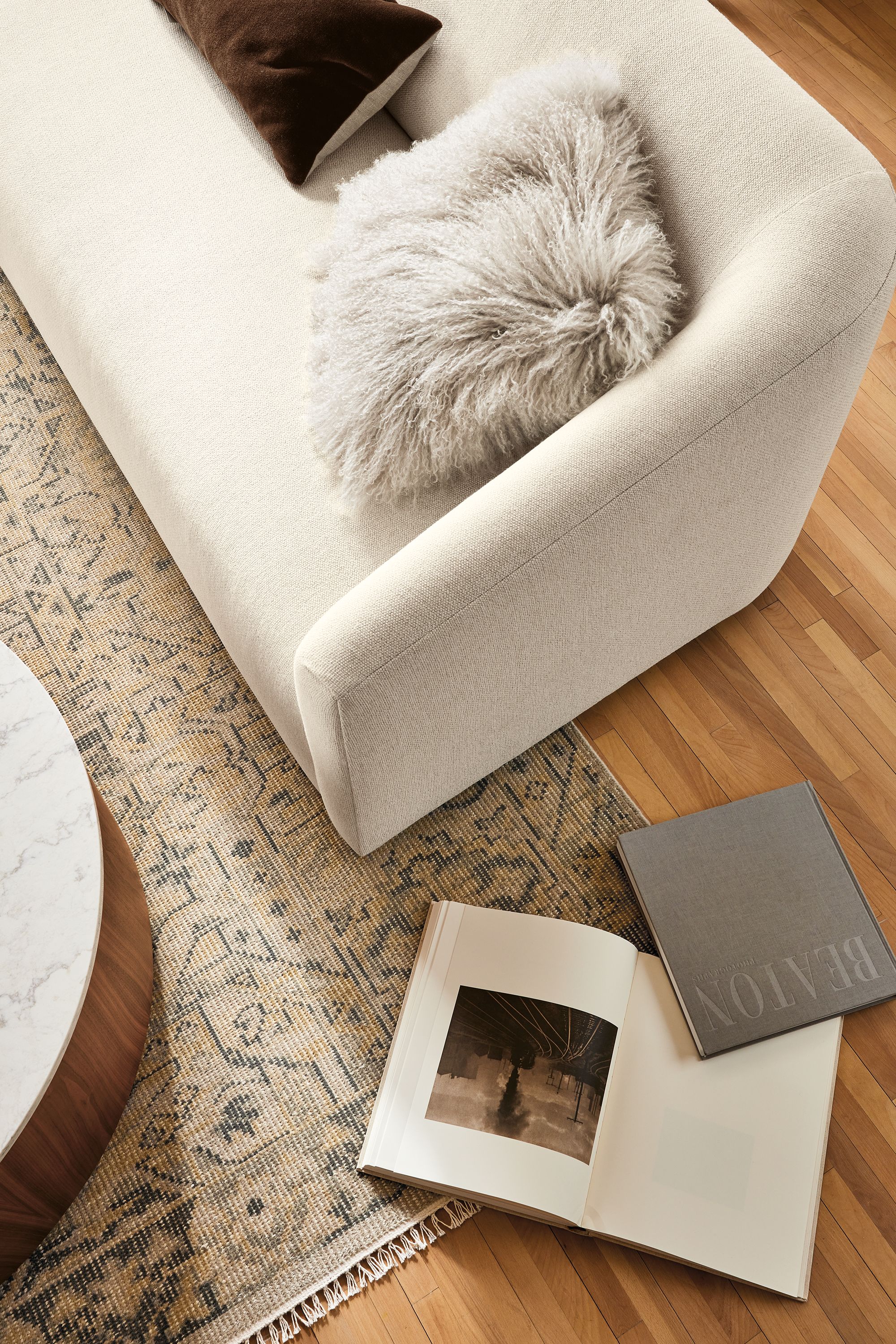 Living room with overhead view of Ada 90-wide sofa in Tepic Ivory and Tibetan sheepskin throw pillow in birch. Anjora 6 by 9 rug in grey-maize.