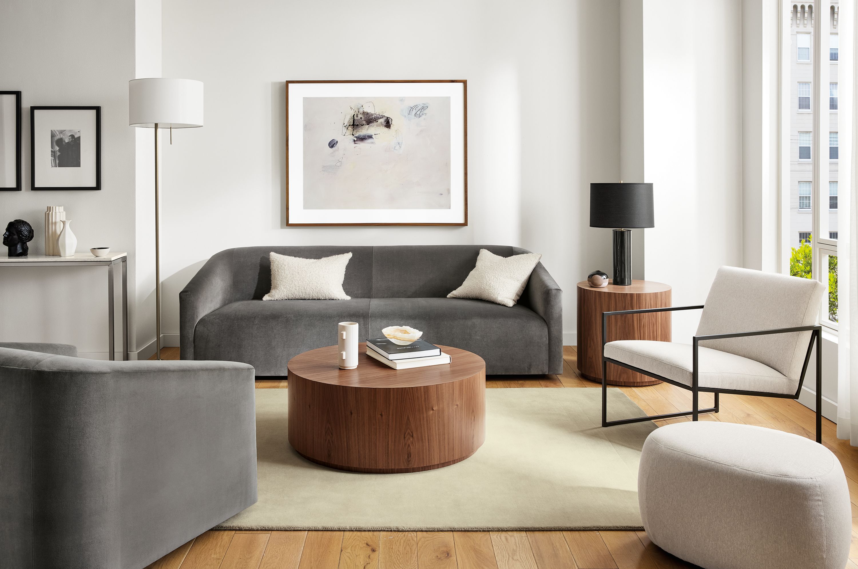 Living room with 90-wide ada sofa in vance gray fabric, ada swivel chair, novato chair, liam wood veneer accent tables.