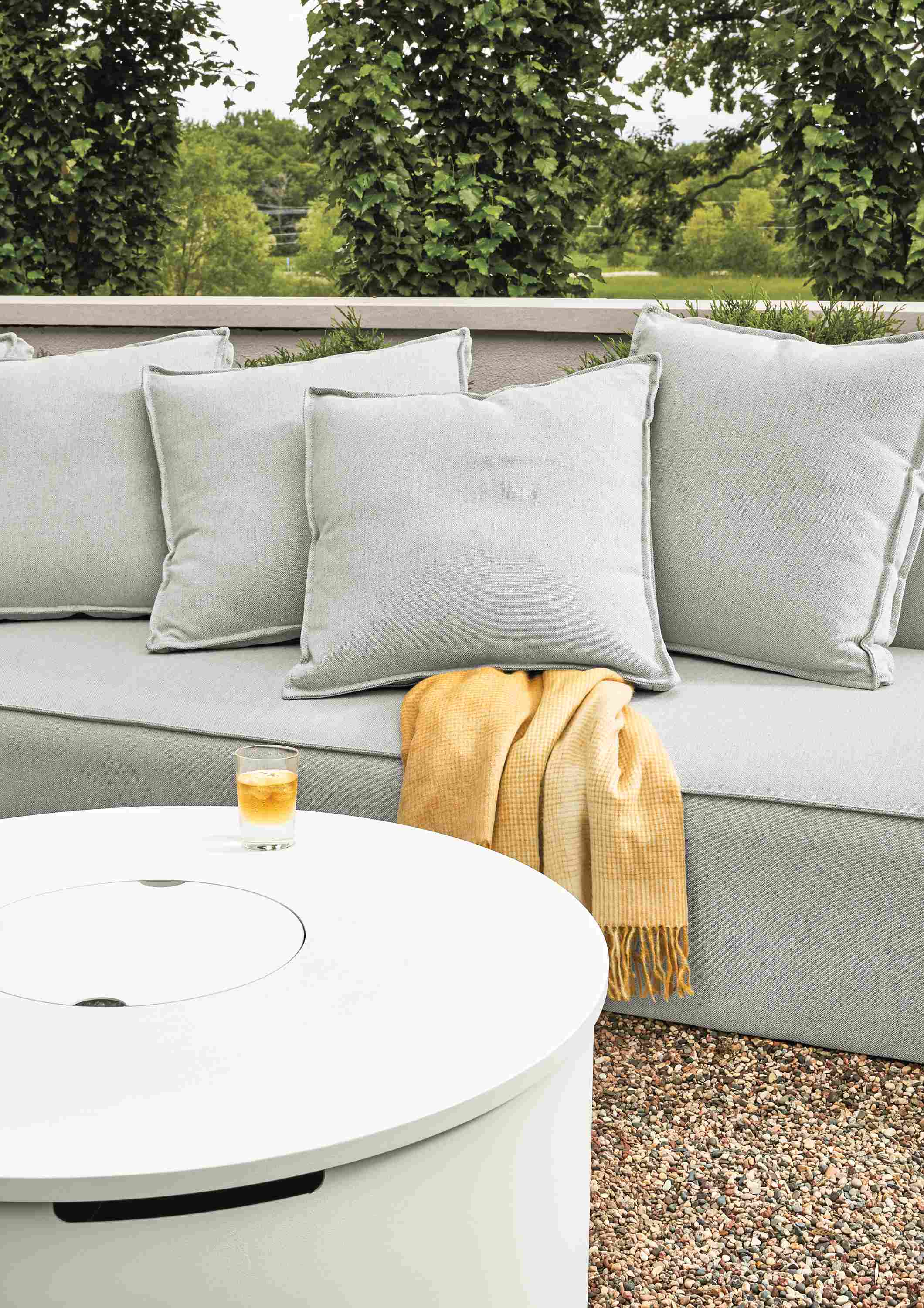 Detail of Adara round fire table in white and Oasis armless sofa in Mist Grey on a patio.