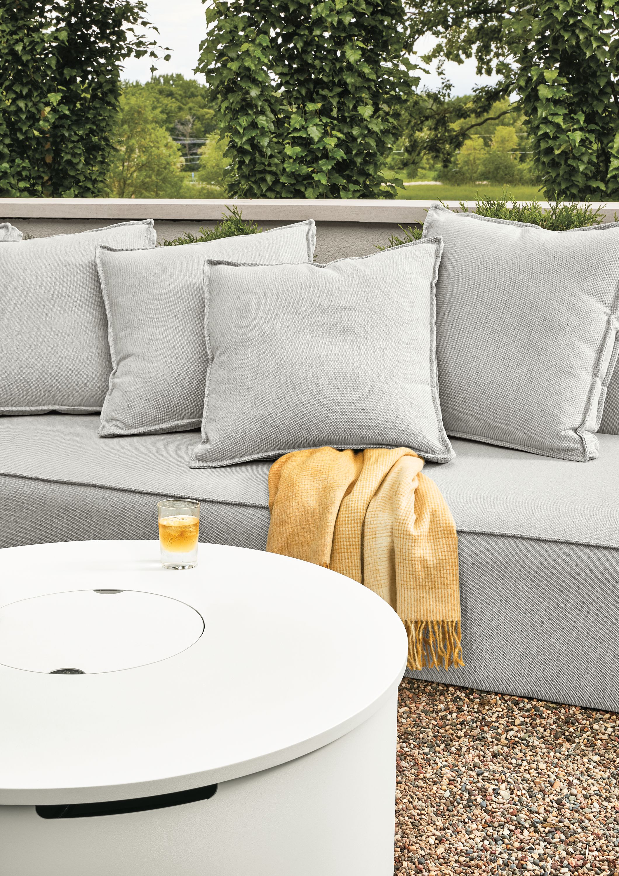 Detail of Adara round fire table in white and Oasis armless sofa in Mist Grey on a patio.