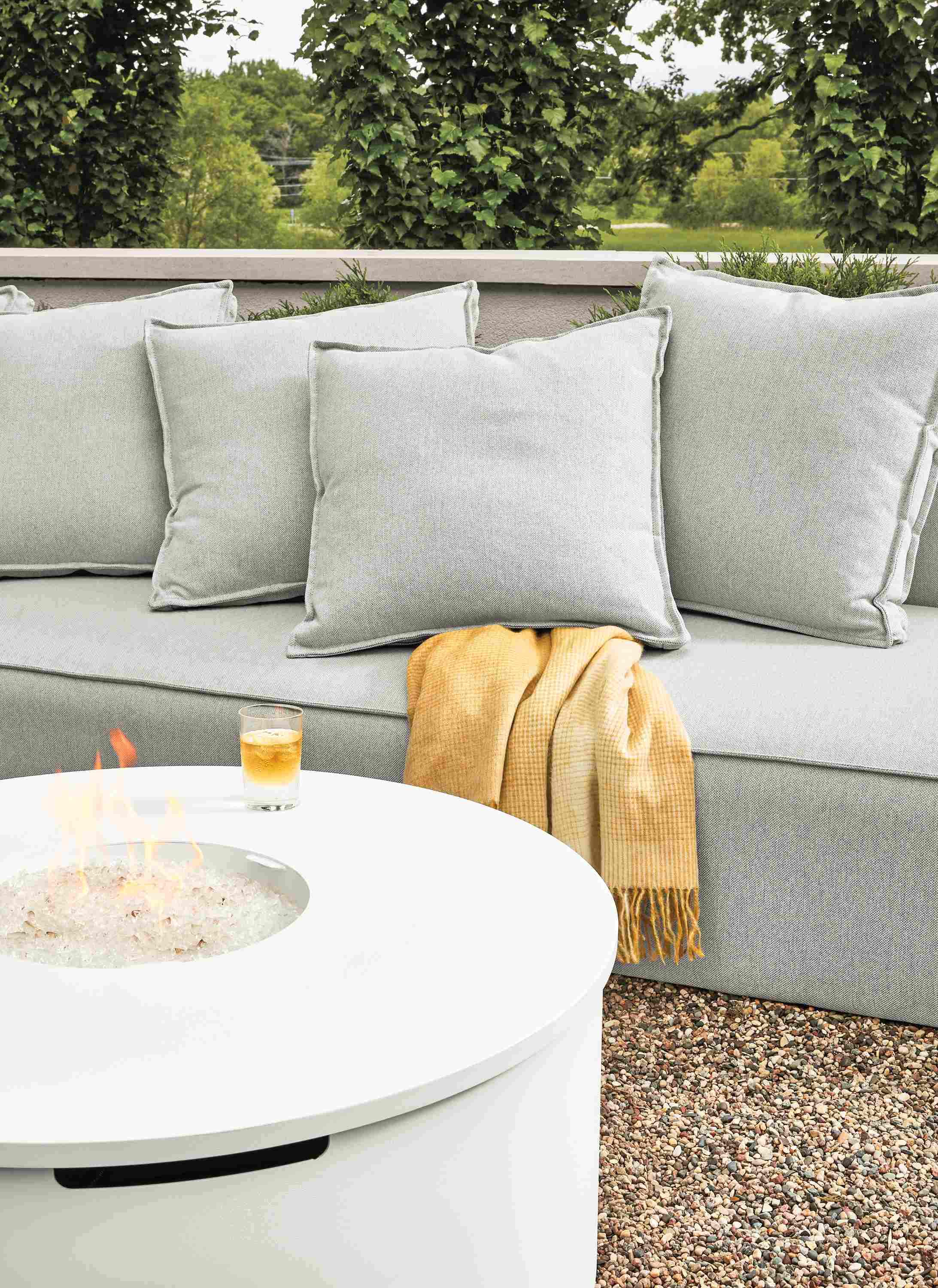 Detail of a lit Adara round fire table in white and Oasis sofa in Mist Grey on a patio.