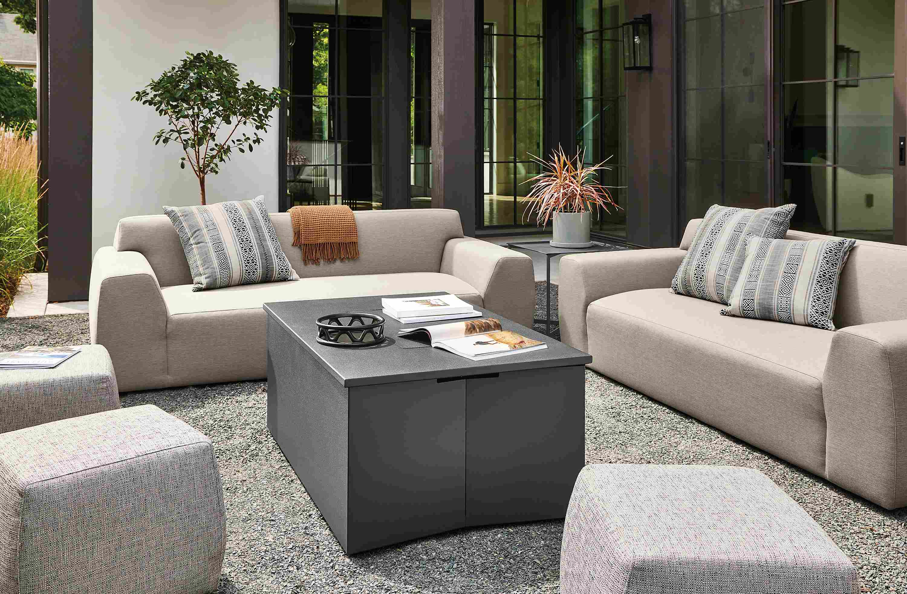 Outdoor seating areas with Adara fire table in graphite, Drift sofas in Pelham Cement and Boyd ottomans in Phipps Charcoal.