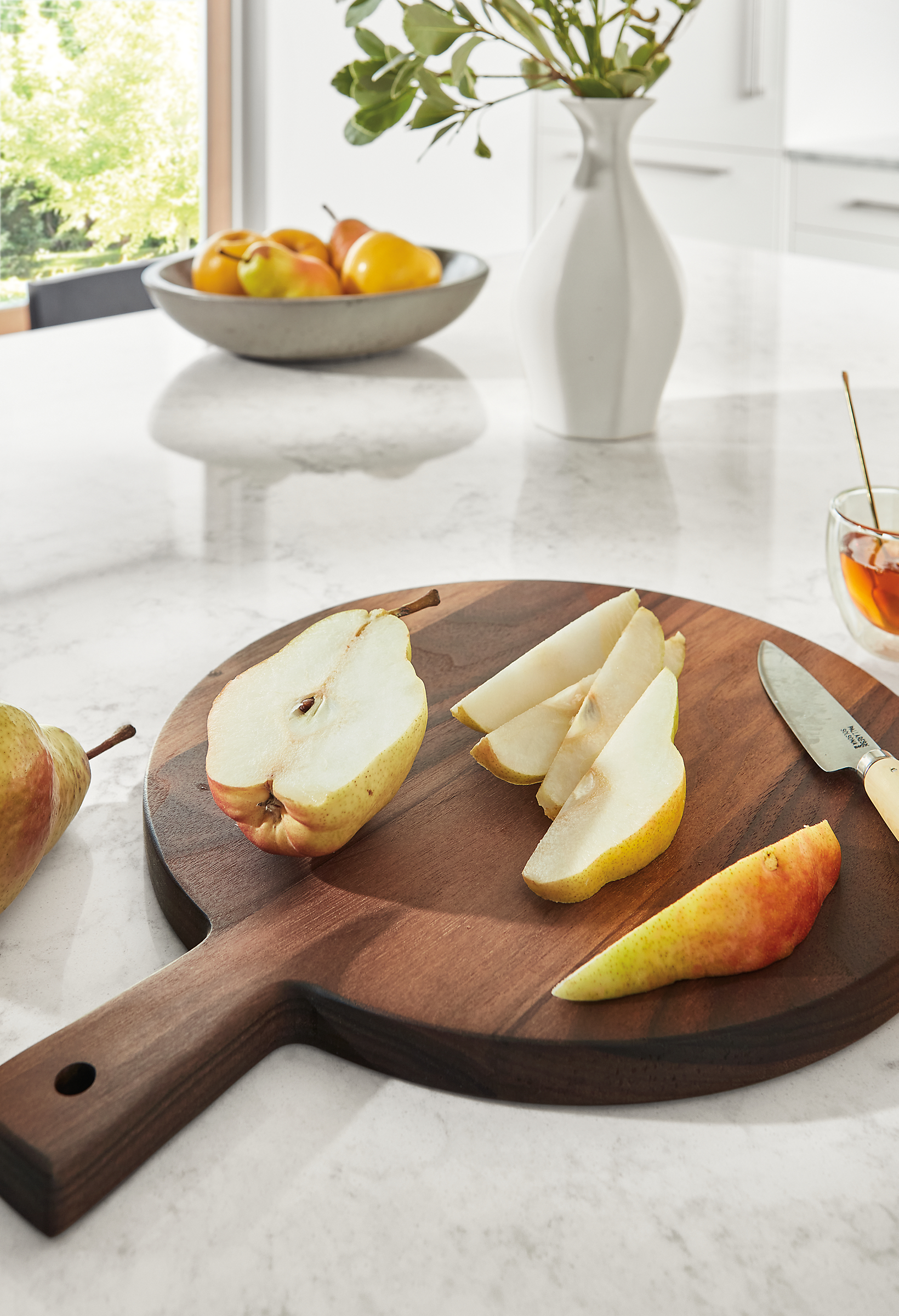 Addy 11-inch diameter serving board in walnut on marbled white quartz counter and Pavo bowl in grey.