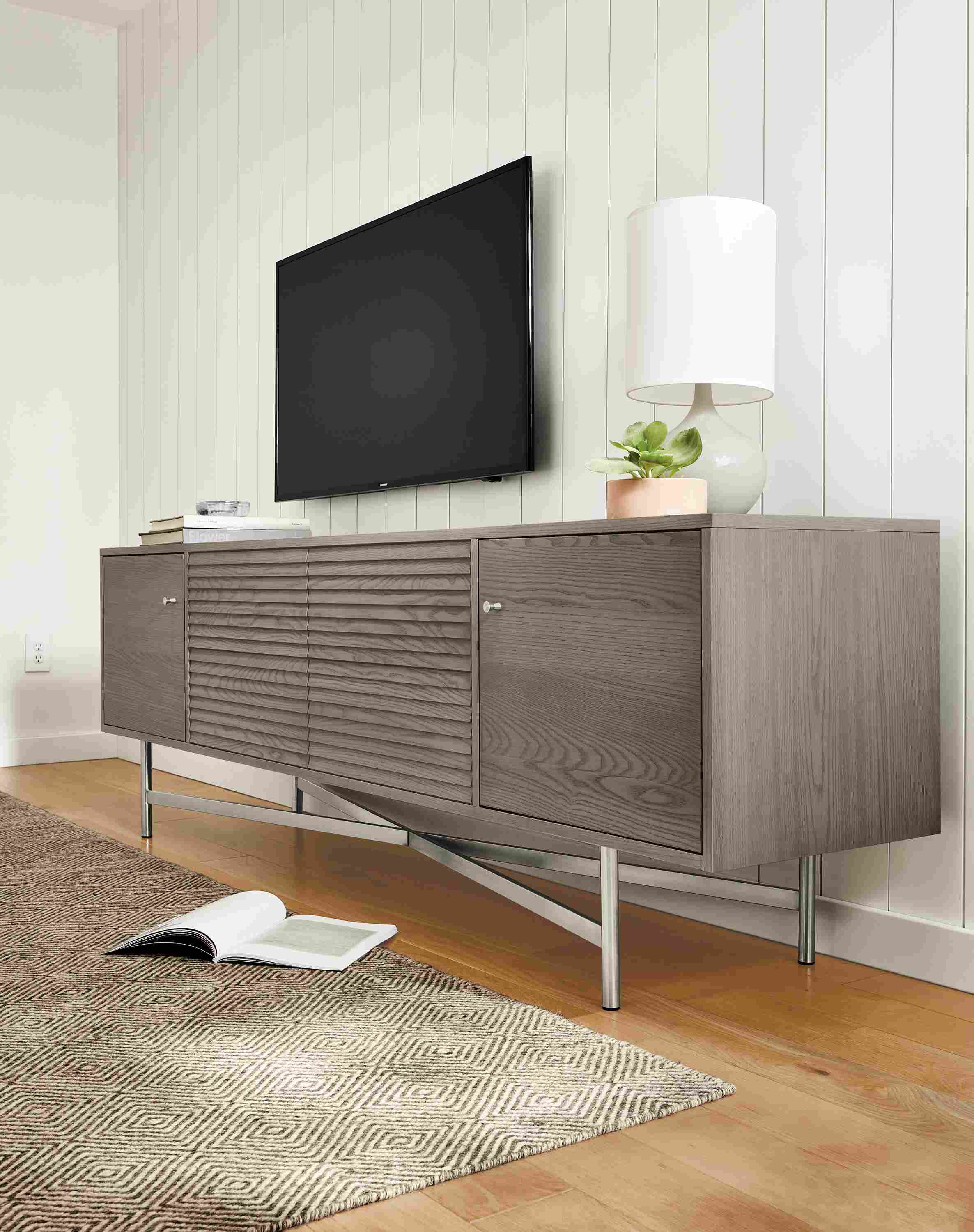 Living room with an angled view of an Adrian 84-wide media cabinet in shell with stainless steel legs.