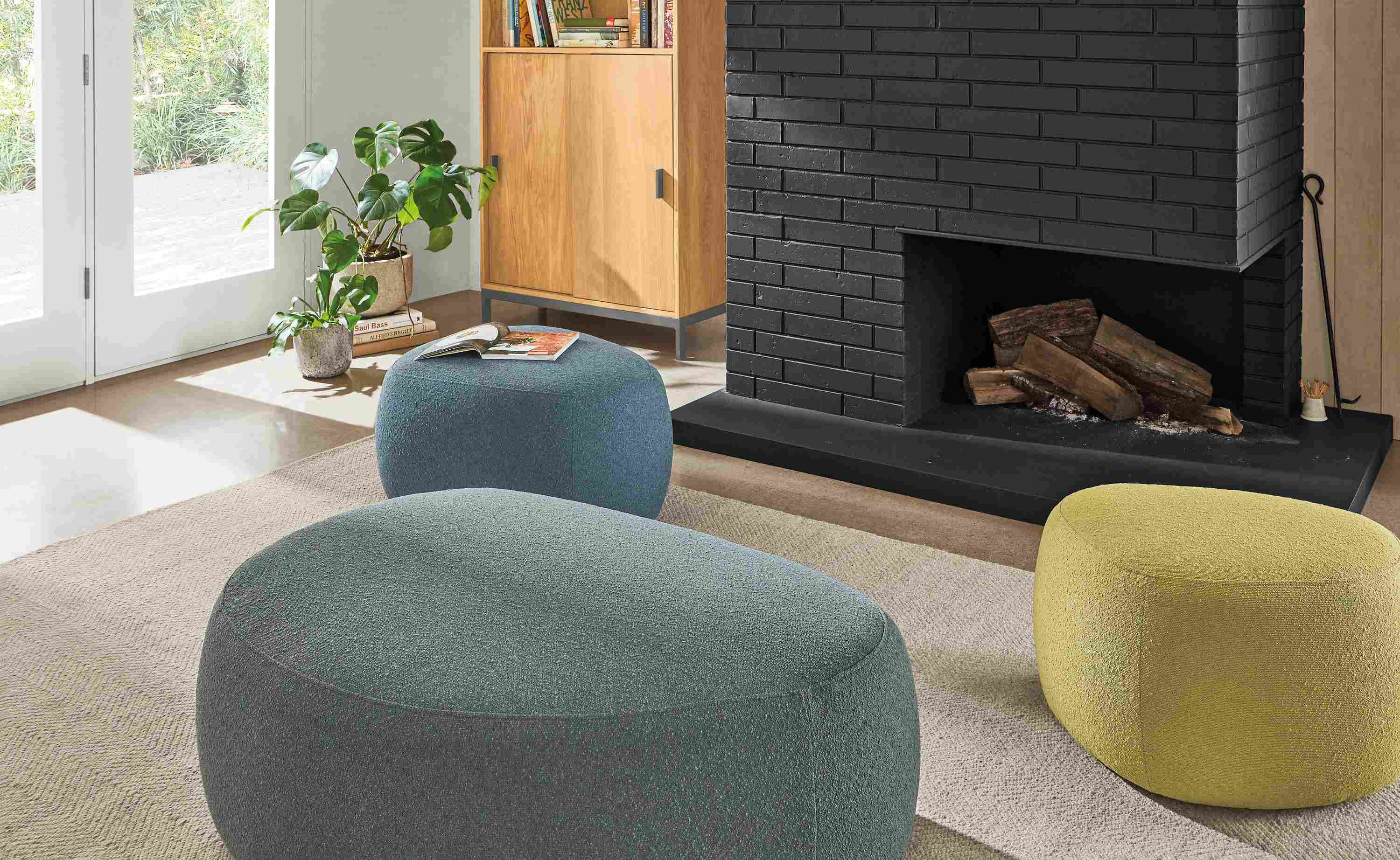 Detail of 3 Asher ottomans in Declan haze, moss and ocean fabrics beside a fireplace.