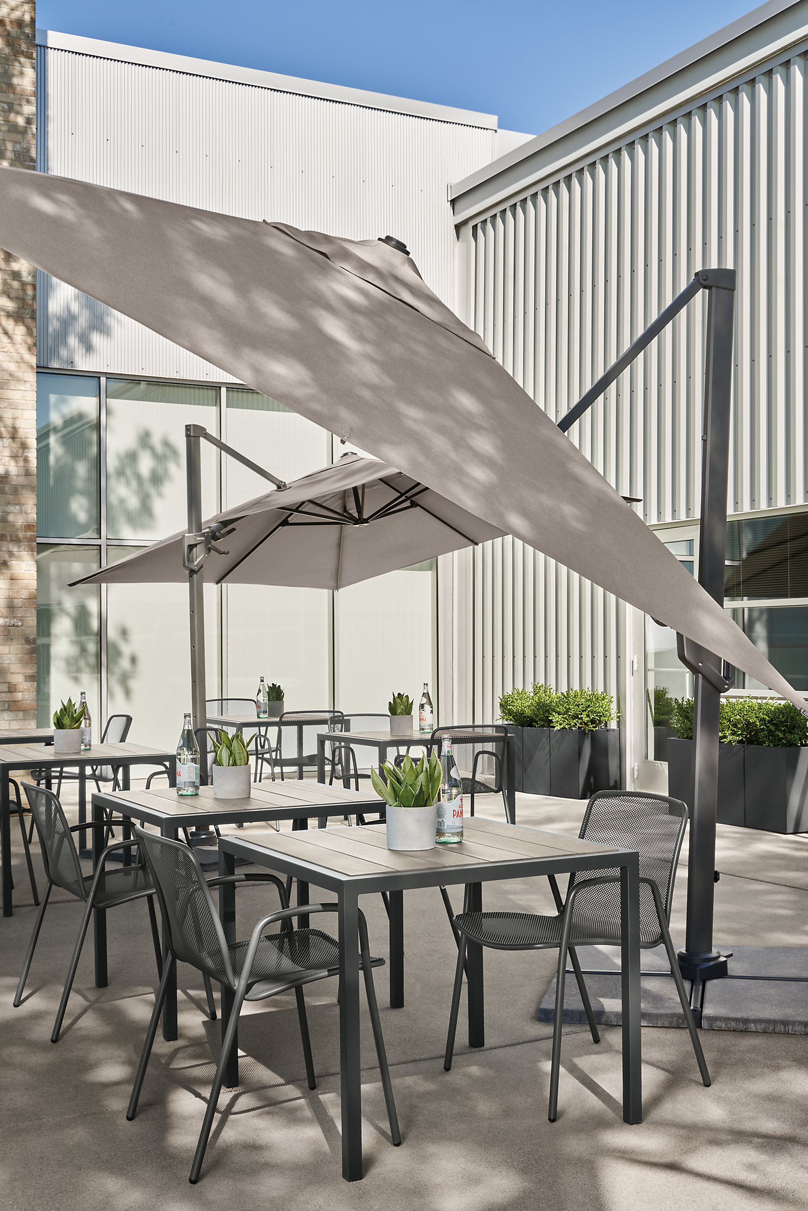 outdoor dining area with alto patio umbrellas tilted, montego tables in aged ash, aruba chairs.
