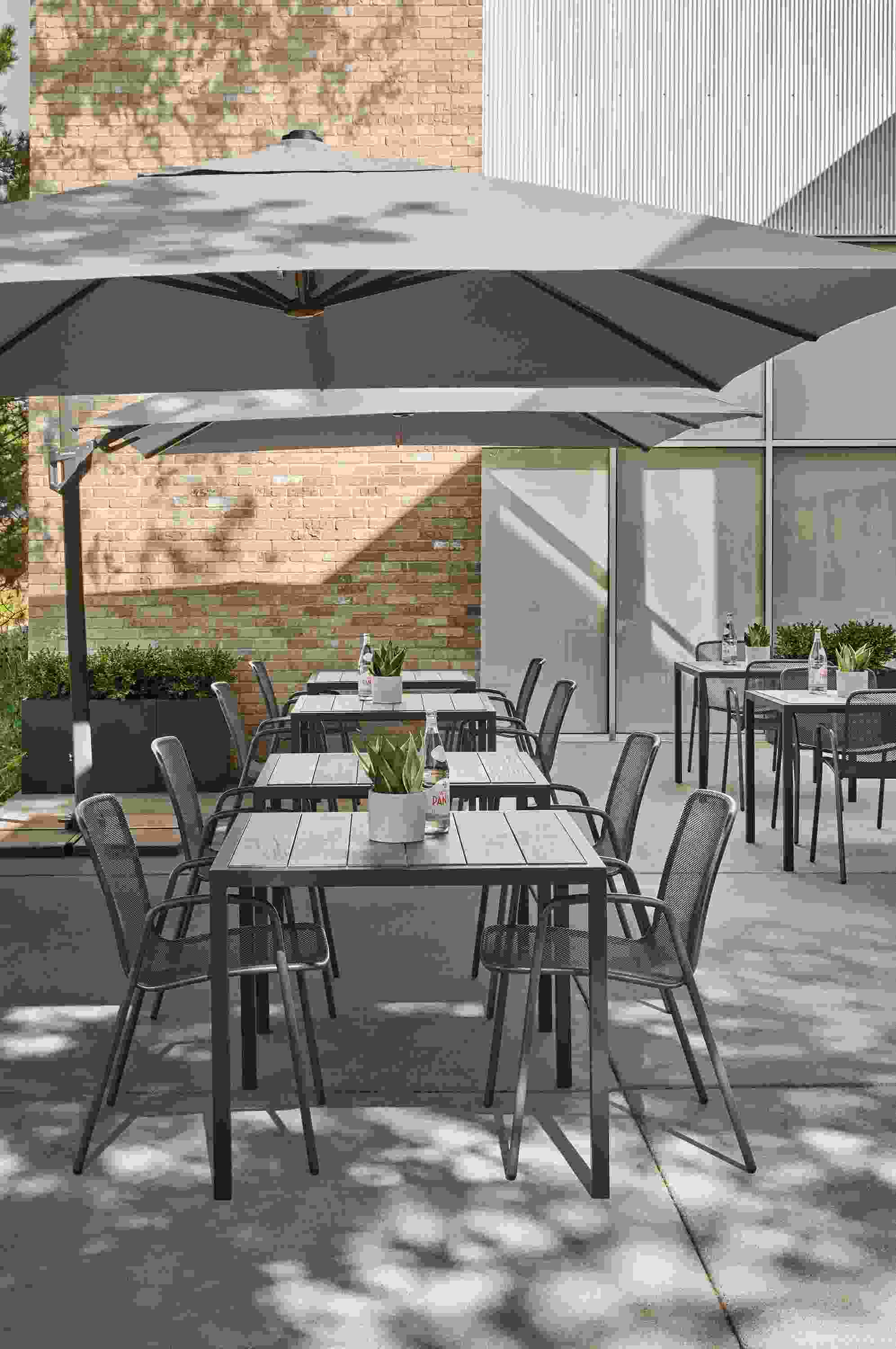 Outdoor dining area with Alto patio umbrellas in Suva taupe, Montego tables in aged ash and Aruba chairs in graphite.
