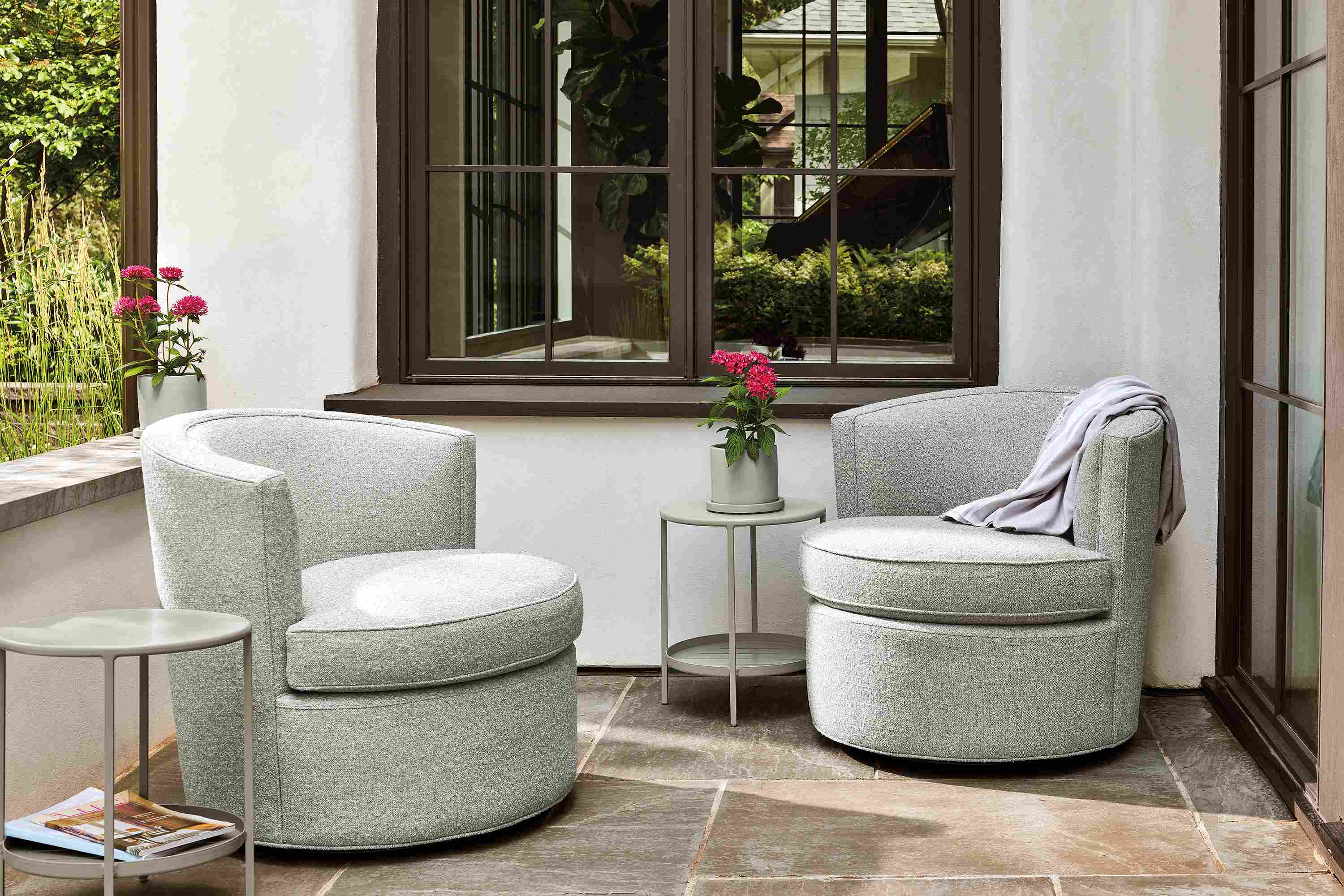 Outdoor patio space with 2 Ambrose swivel chairs in Kloss Cadet fabric and a slim round outdoor side table in taupe.