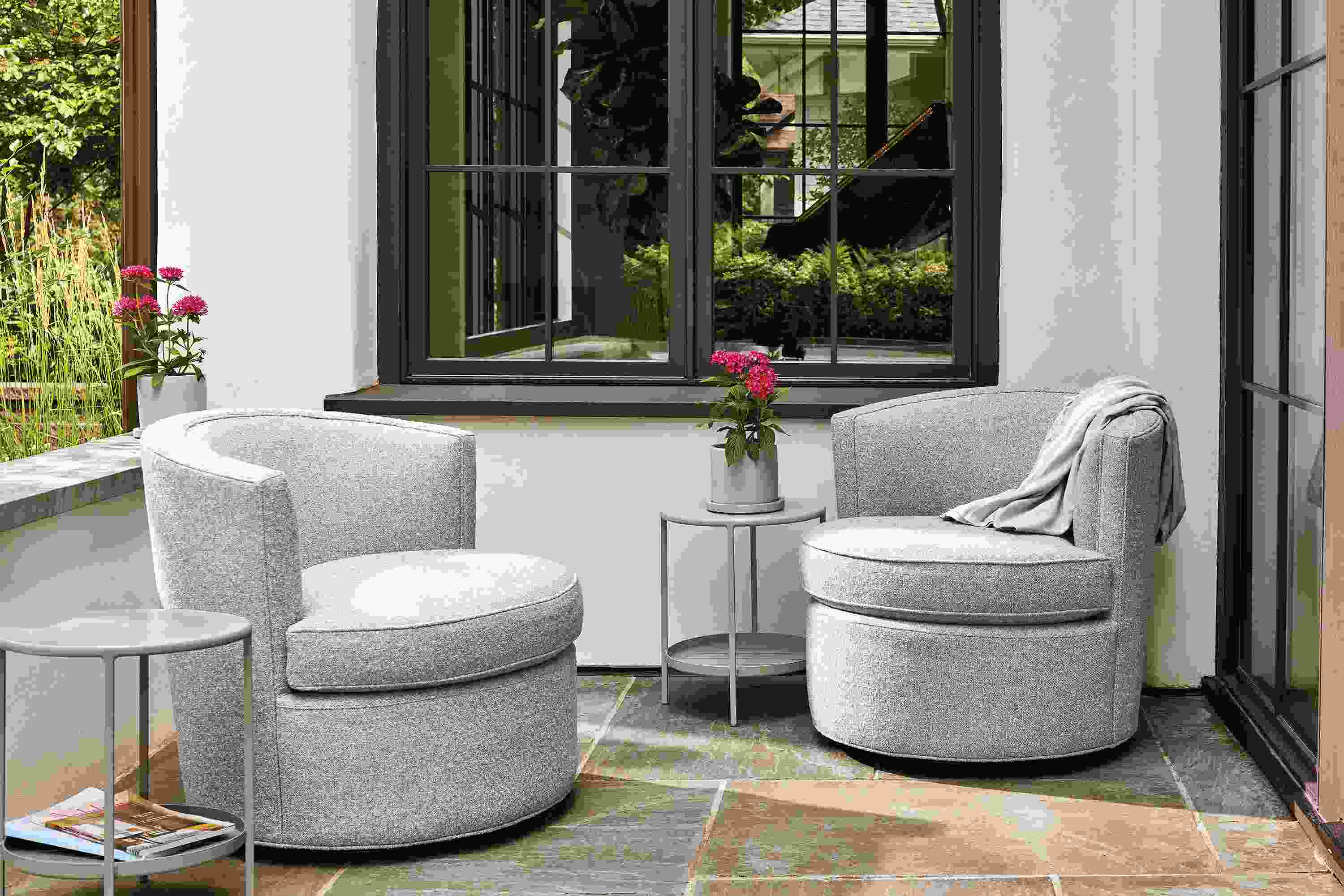 Outdoor patio space with 2 Ambrose swivel chairs in Kloss Cadet fabric and a slim round outdoor side table in taupe.