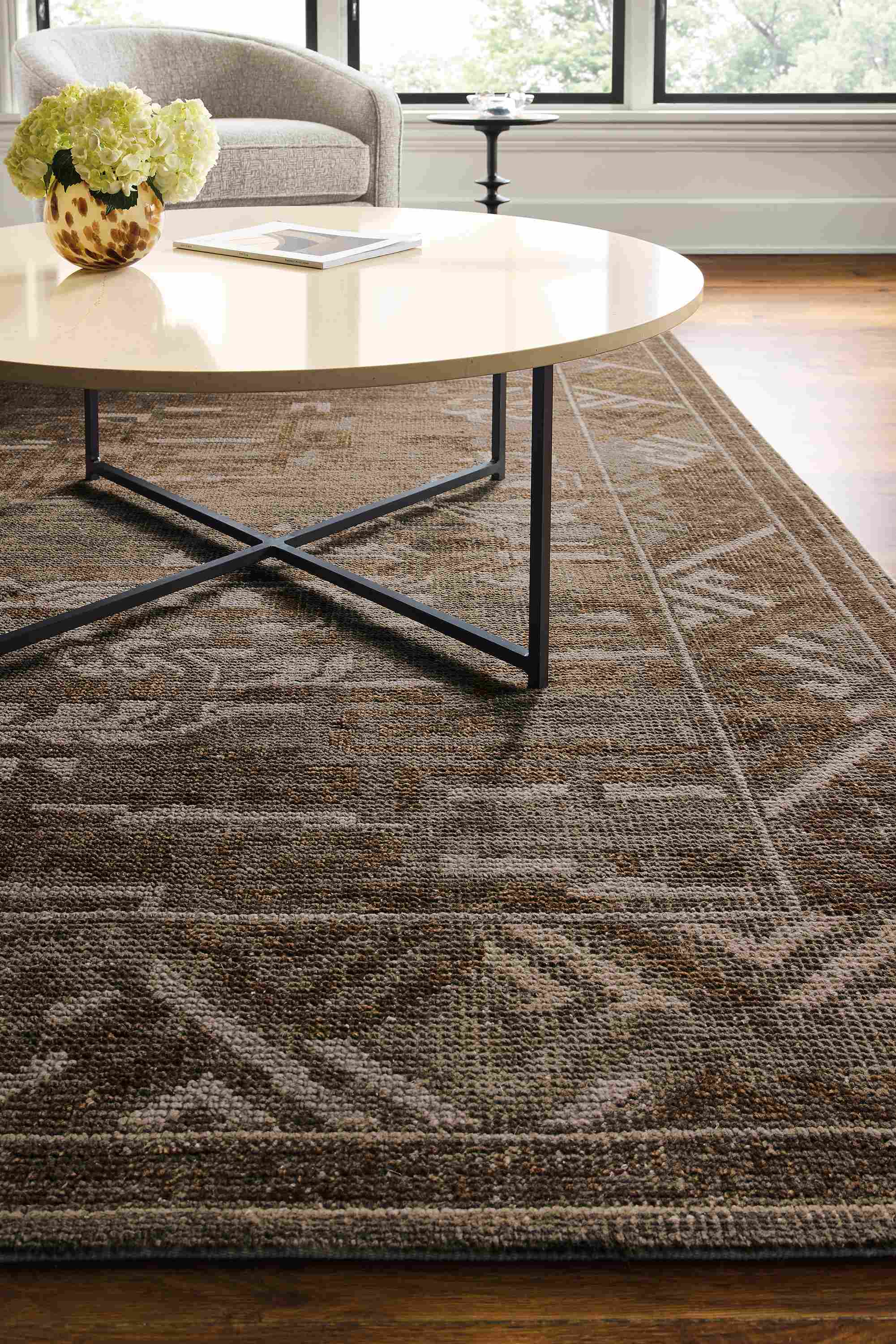 Living room with detail of amira 8 by 10 rug in earth and classic 42-round diameter coffee table in natural steel with ecru quartz top.