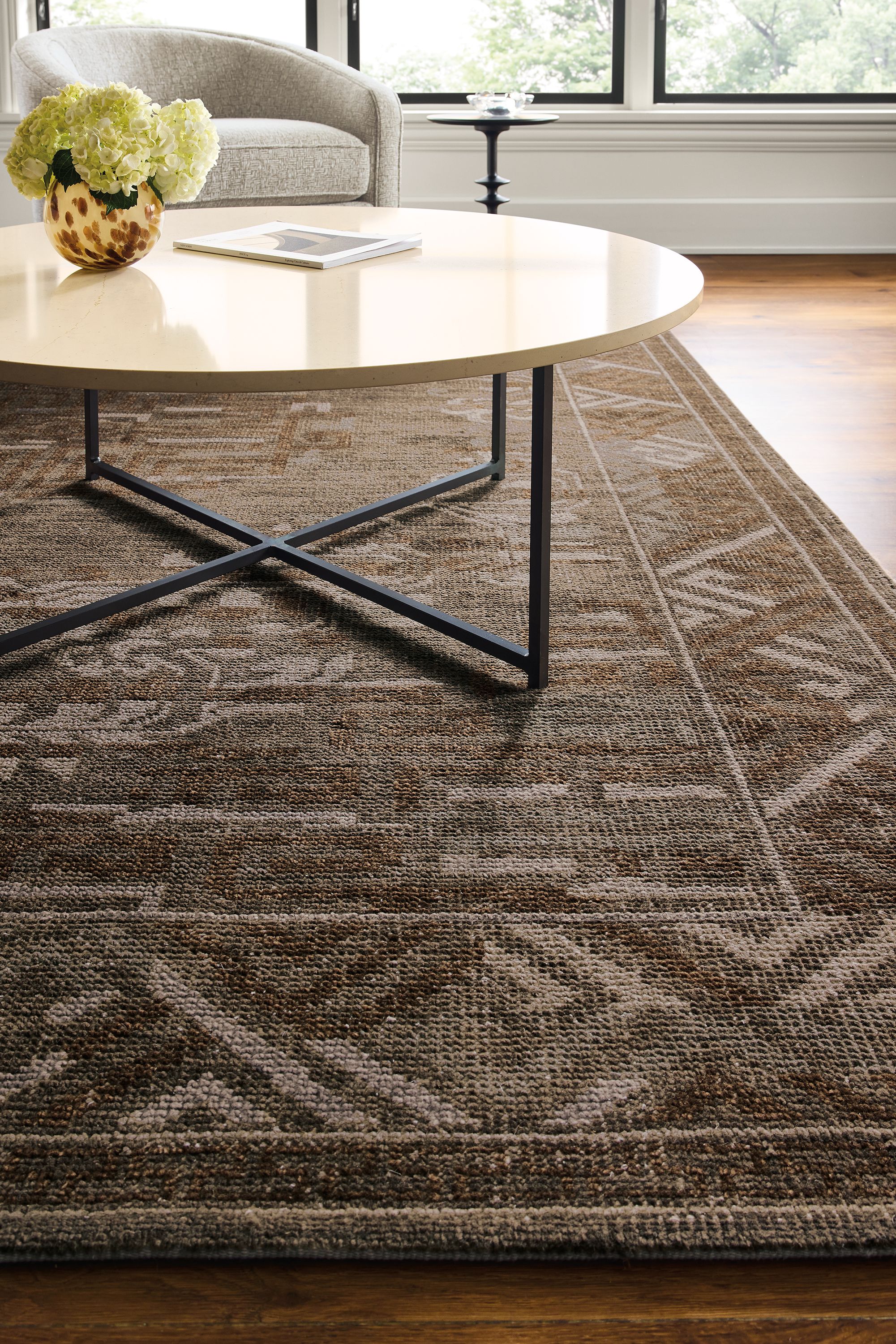 Living room with detail of amira 8 by 10 rug in earth and classic 42-round diameter coffee table in natural steel with ecru quartz top.