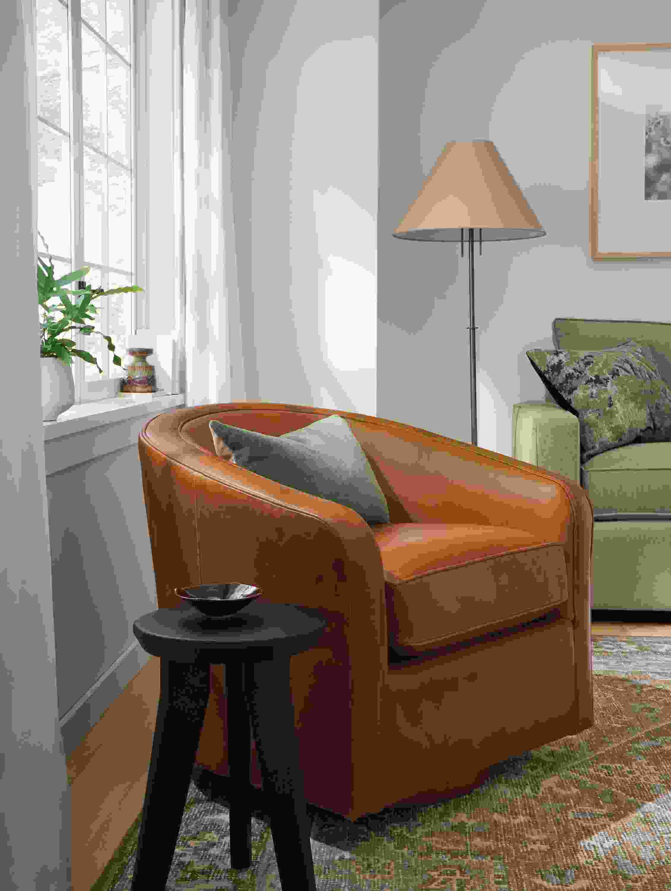 Living room with Amos swivel chair in Vento Cognac leather, Veda rug in Moss and Hollins stool in reclaimed charcoal pine.