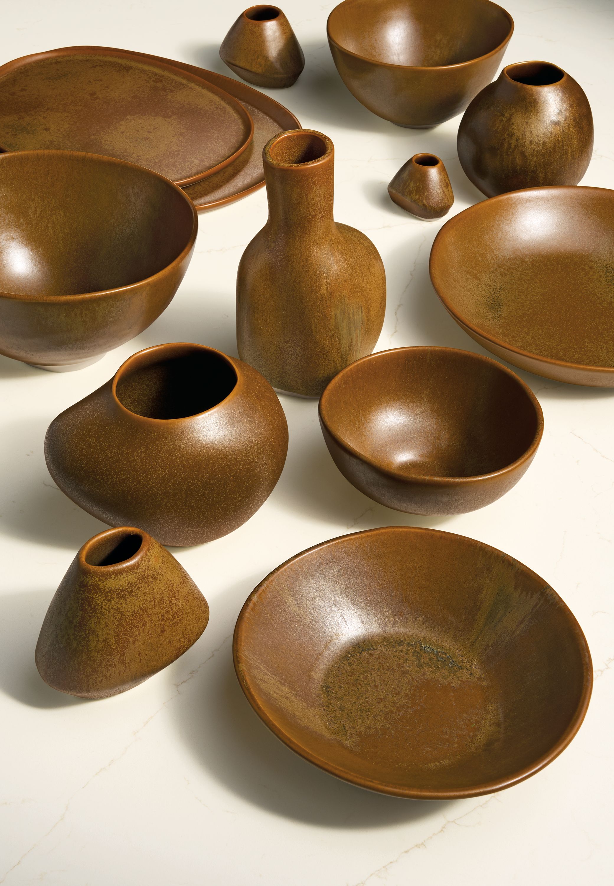 Group shot of Anya, Ripple and Nadia bowls, vases and trays all in rust on a marbled ivory quartz top.