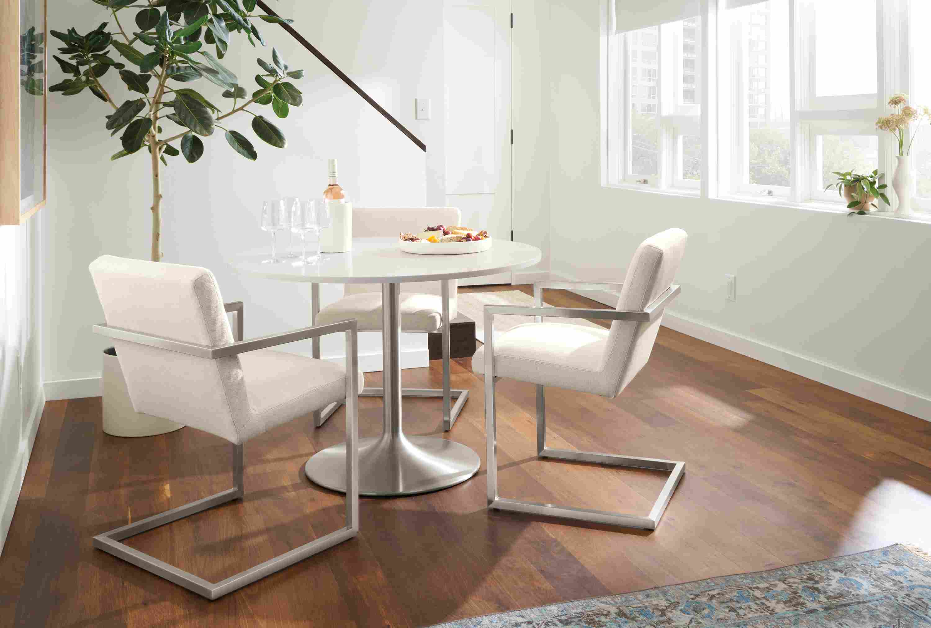Dining nook with Aria round table in stainless steel and Light grey quartz  and 3 Lira arm chairs stainless and Sumner Ivory.