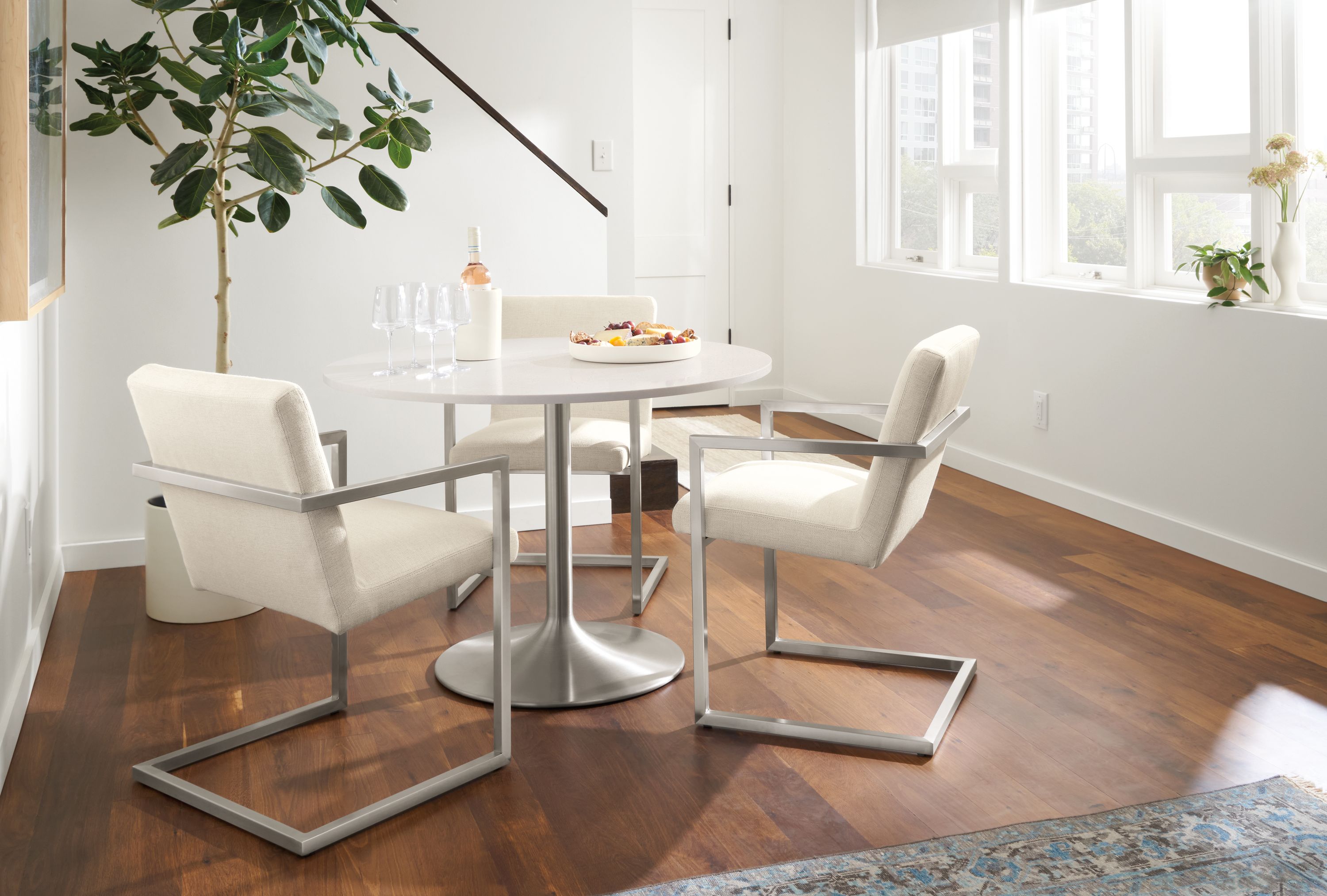 room setting including aria round table and 3 lira arm chairs in white.