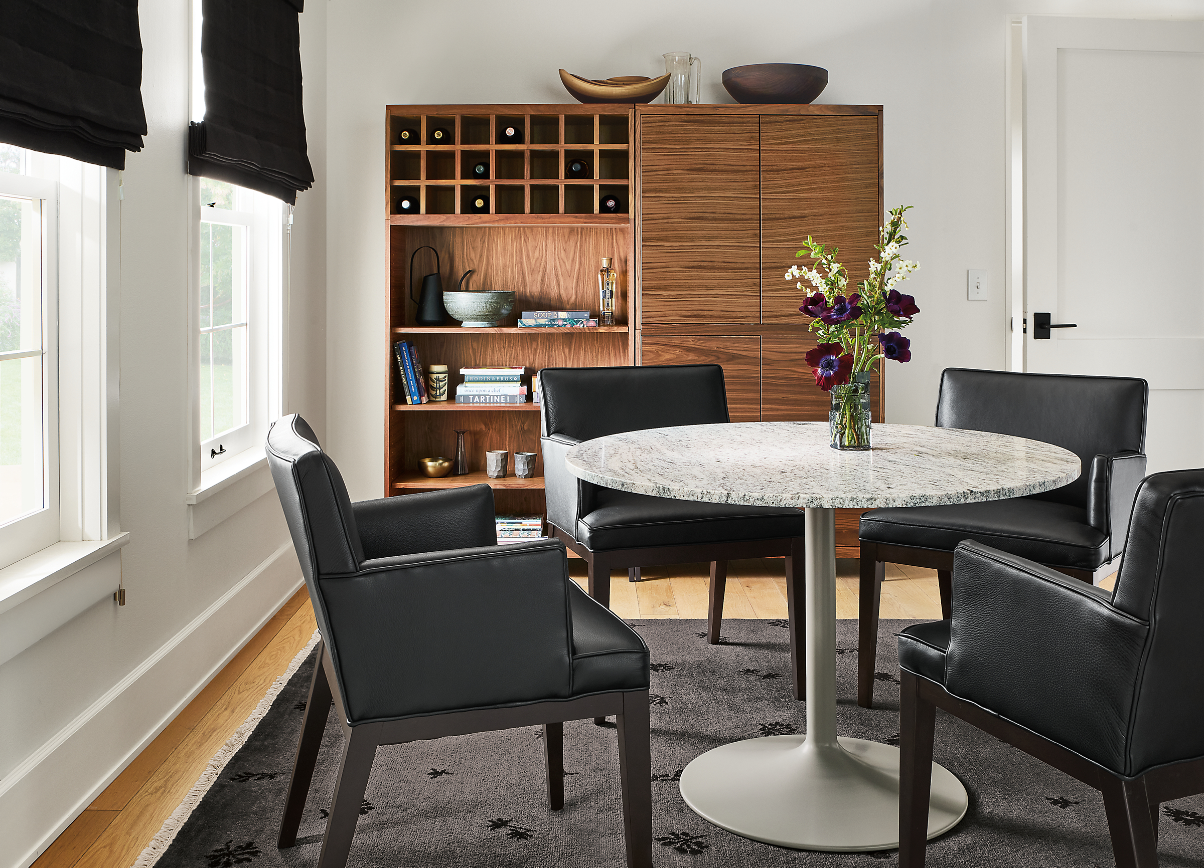 Dining room with Aria 42-Round Dining Table in taupe with Wiscont White Granite top , Ansel Arm Chairs in Urbino Black and Taylor Dining Wall Unit in Walnut with Steel Base.