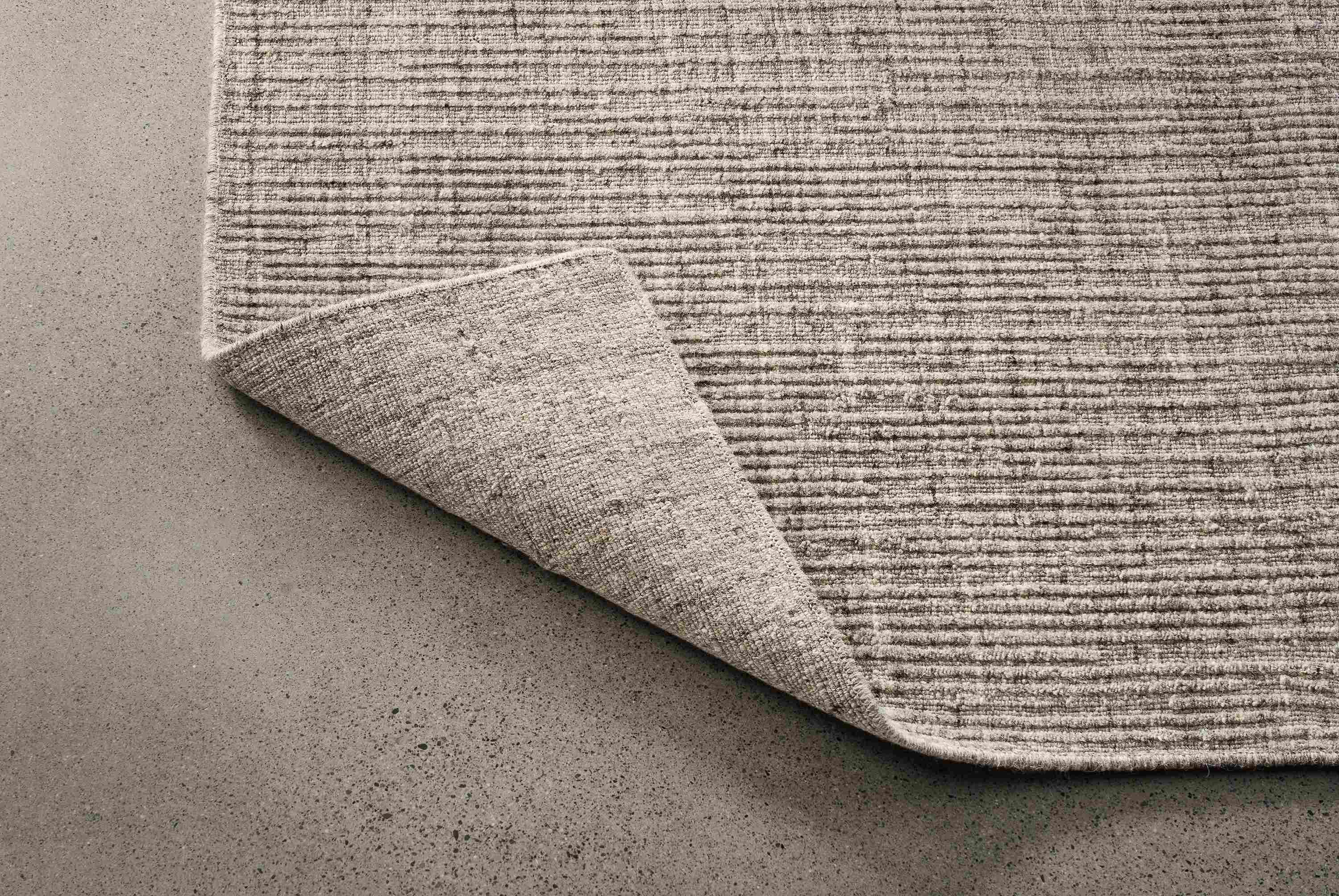 Detail of artis 8 by 10 rug in grey shown with corner turned over to show back side of rug.