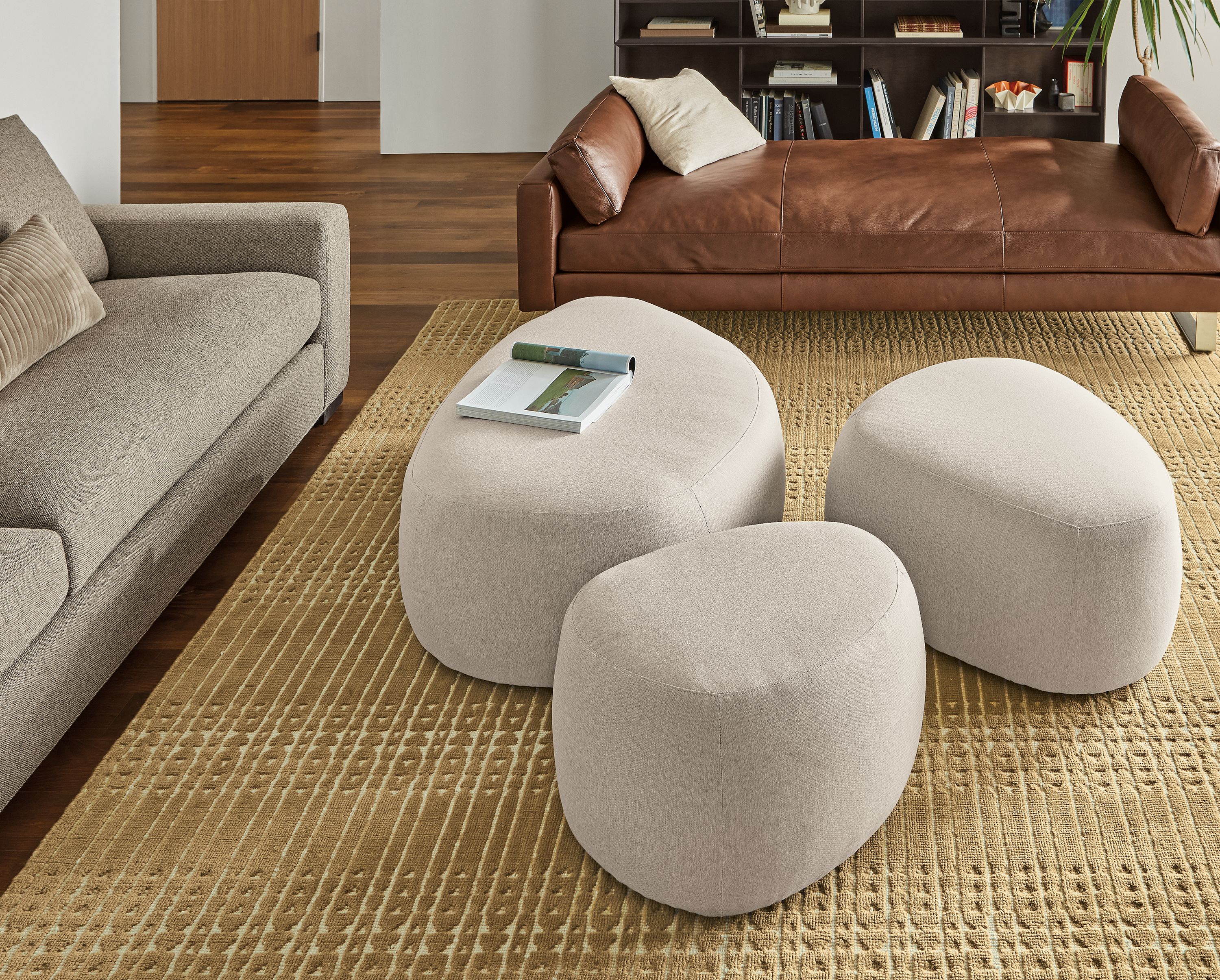 Living area with set of three Asher ottomans in Flint oatmeal, Pierson daybed in Lecco cognac leather and Bria rug in mustard.