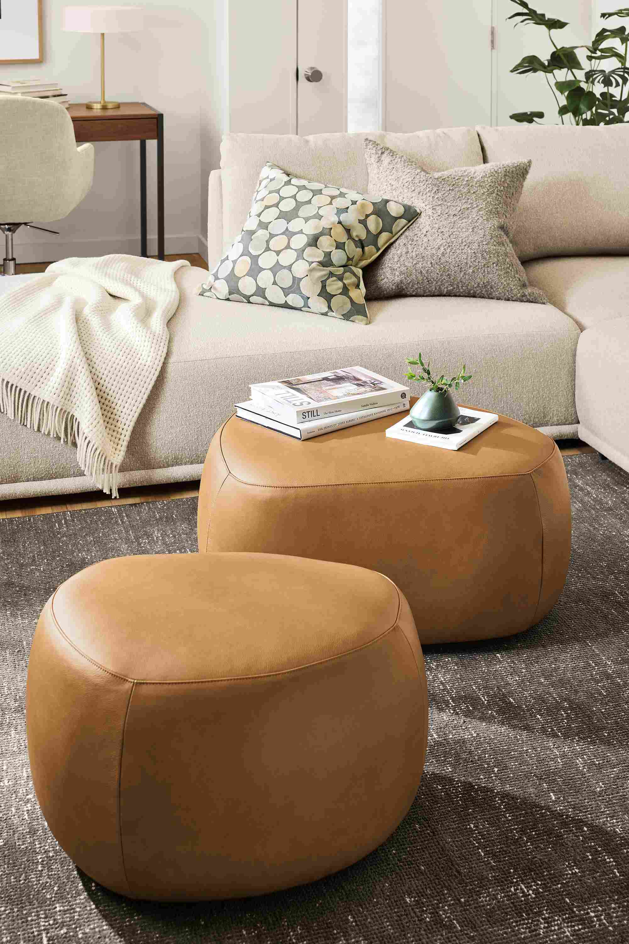 Living room with detail of 2 asher ottomans in laino camel leather, samar rug in charcoal and fia sofa.