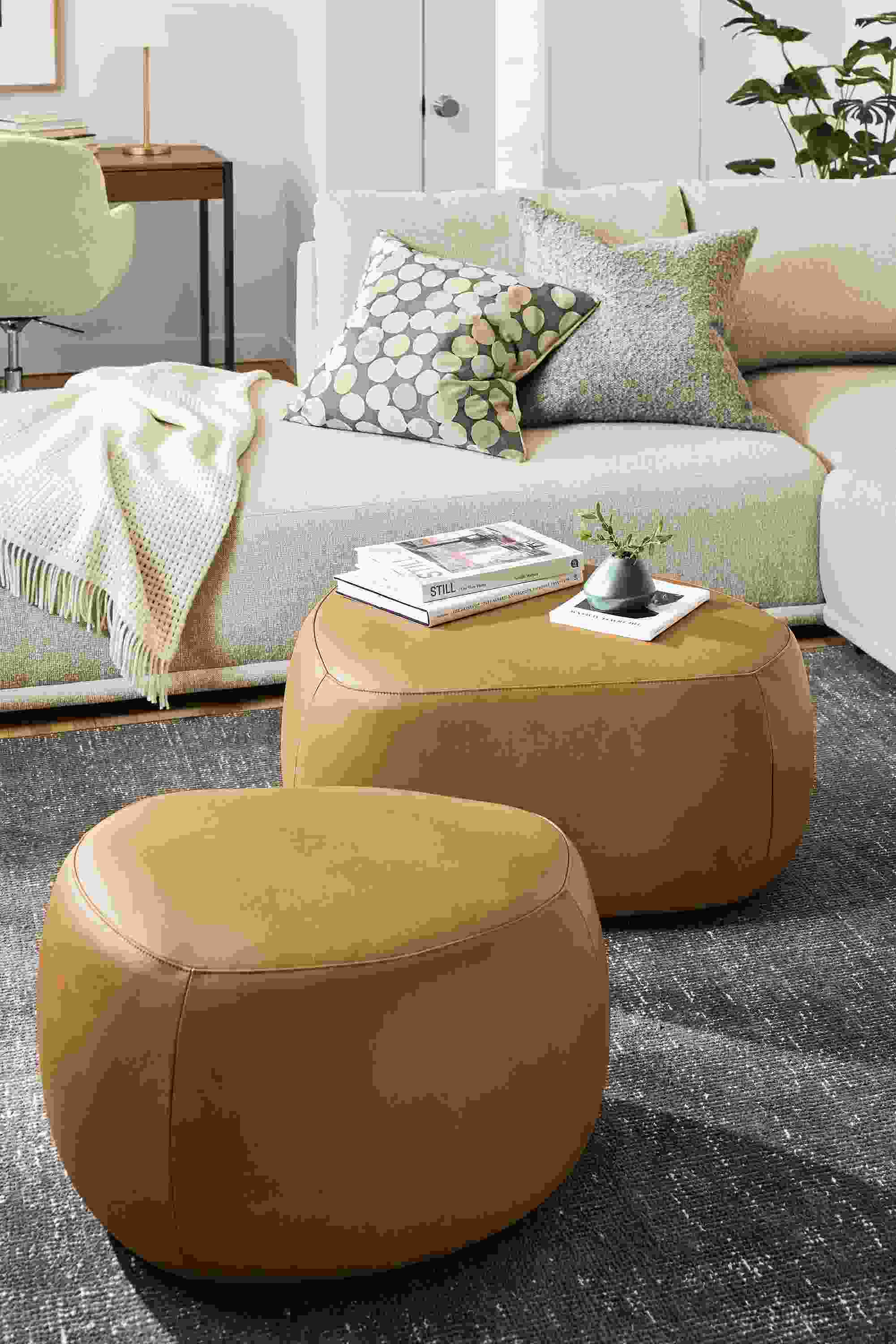 Living room with detail of 2 asher ottomans in laino camel leather, samar rug in charcoal and fia sofa.
