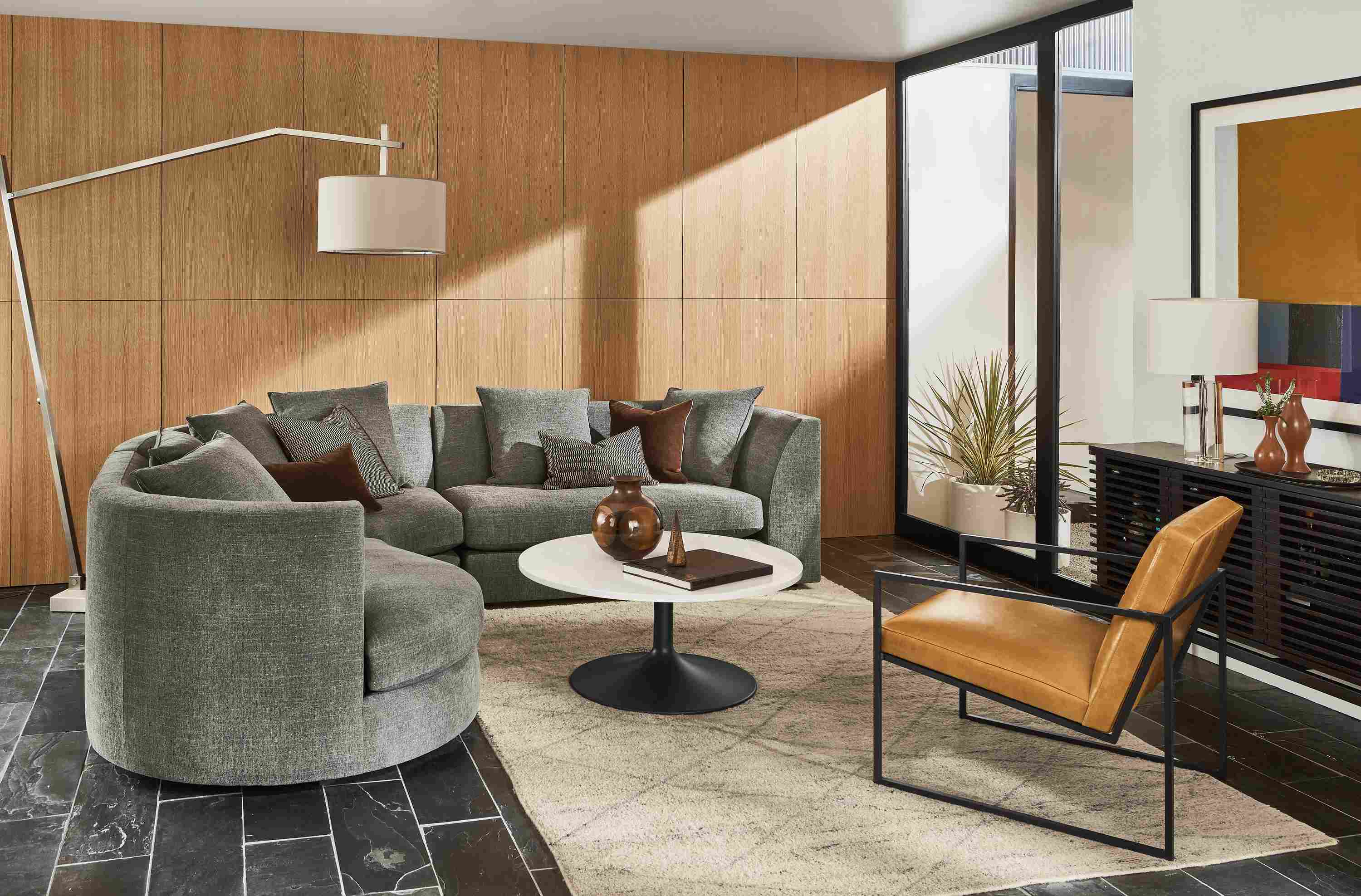 Living room with Astaire 3-piece curved sectional, Novato chair in vento camel leather, Aria coffee table and kalindi rug.
