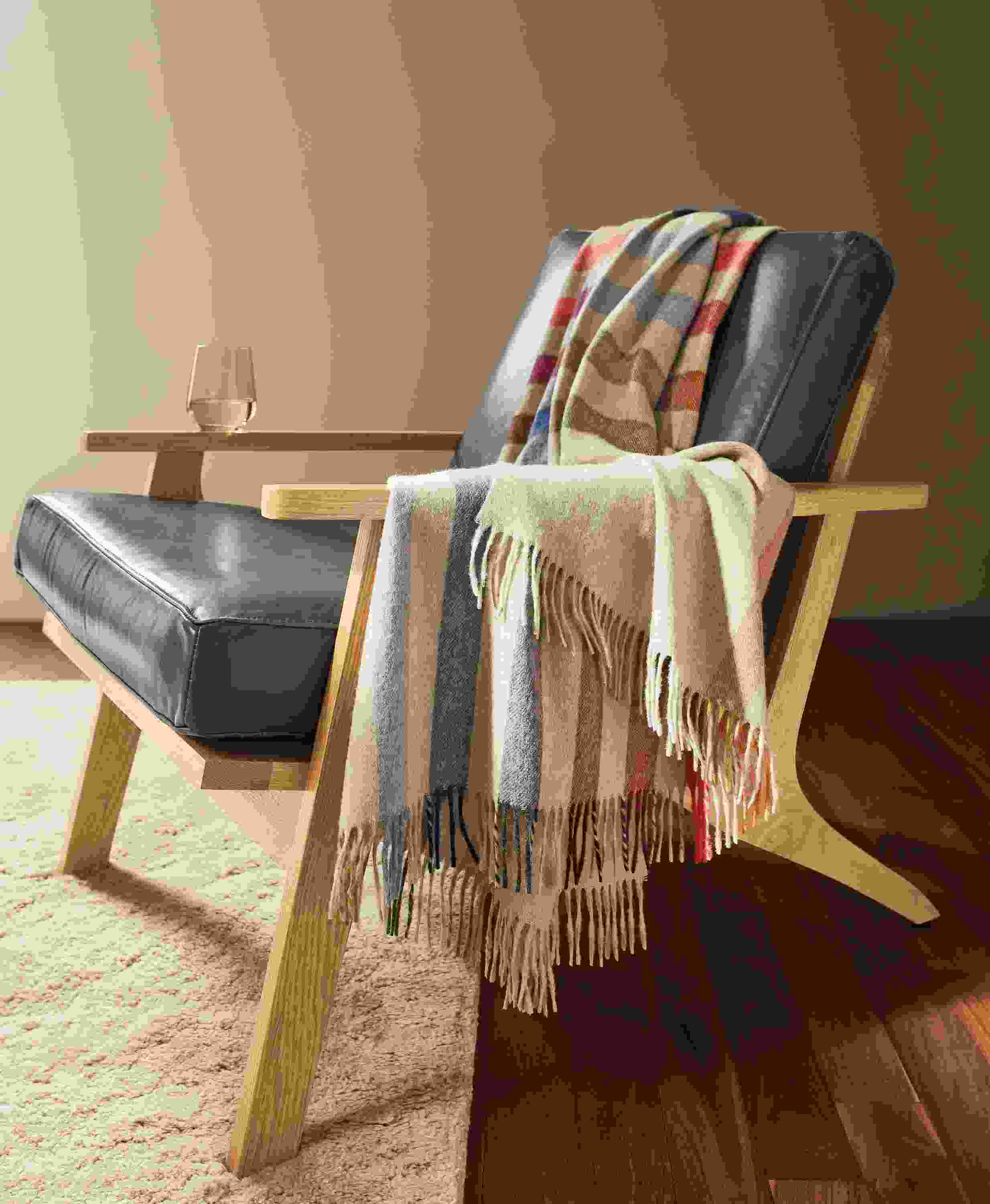 Detail of Audrey multicolor throw blanket draped on a Sanna chair in Vento Smoke leather and white oak.