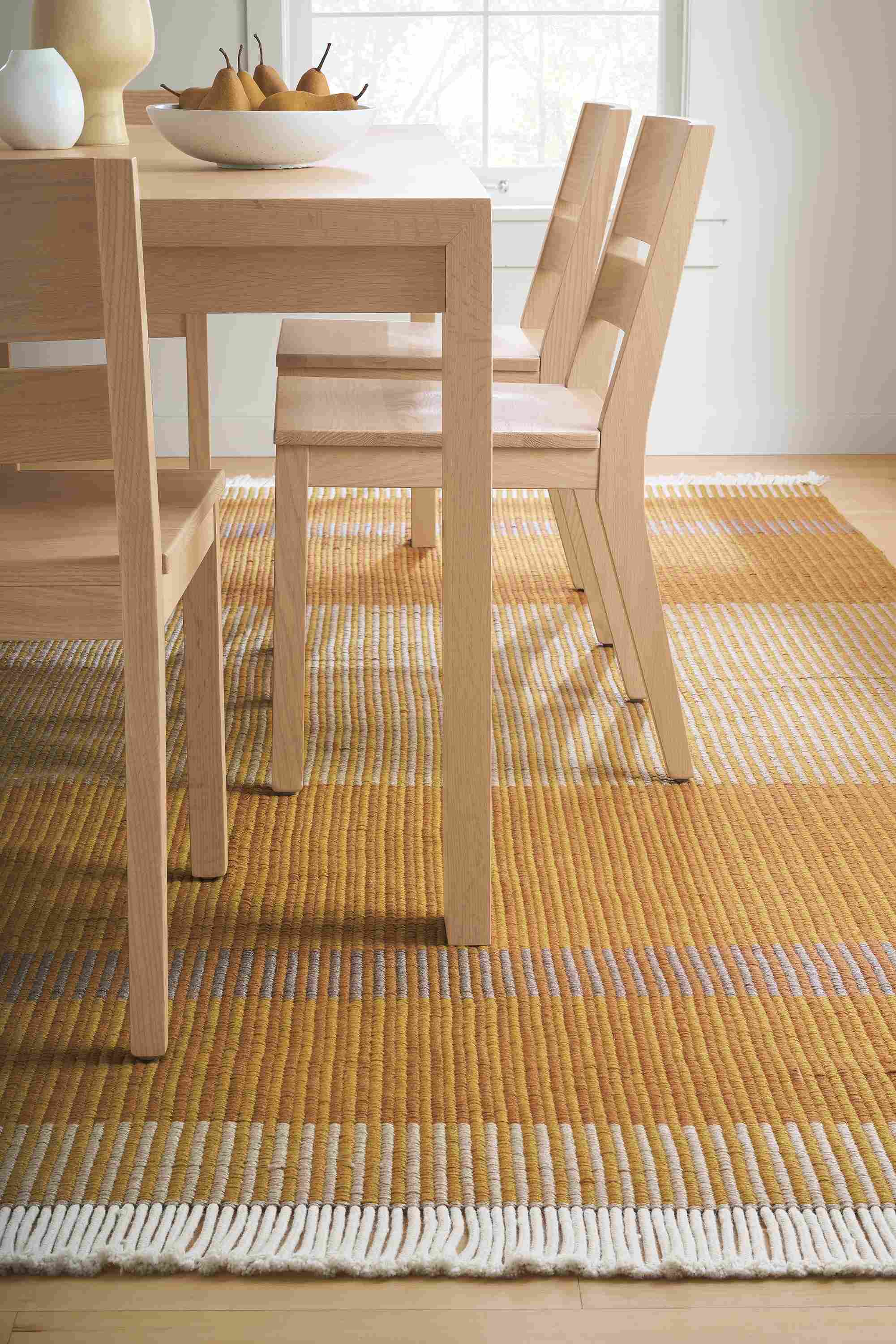 Dining room with detail of Ayla 8 by 10 rug in mustard and Walsh extension table and Afton side chairs in salt on red oak.