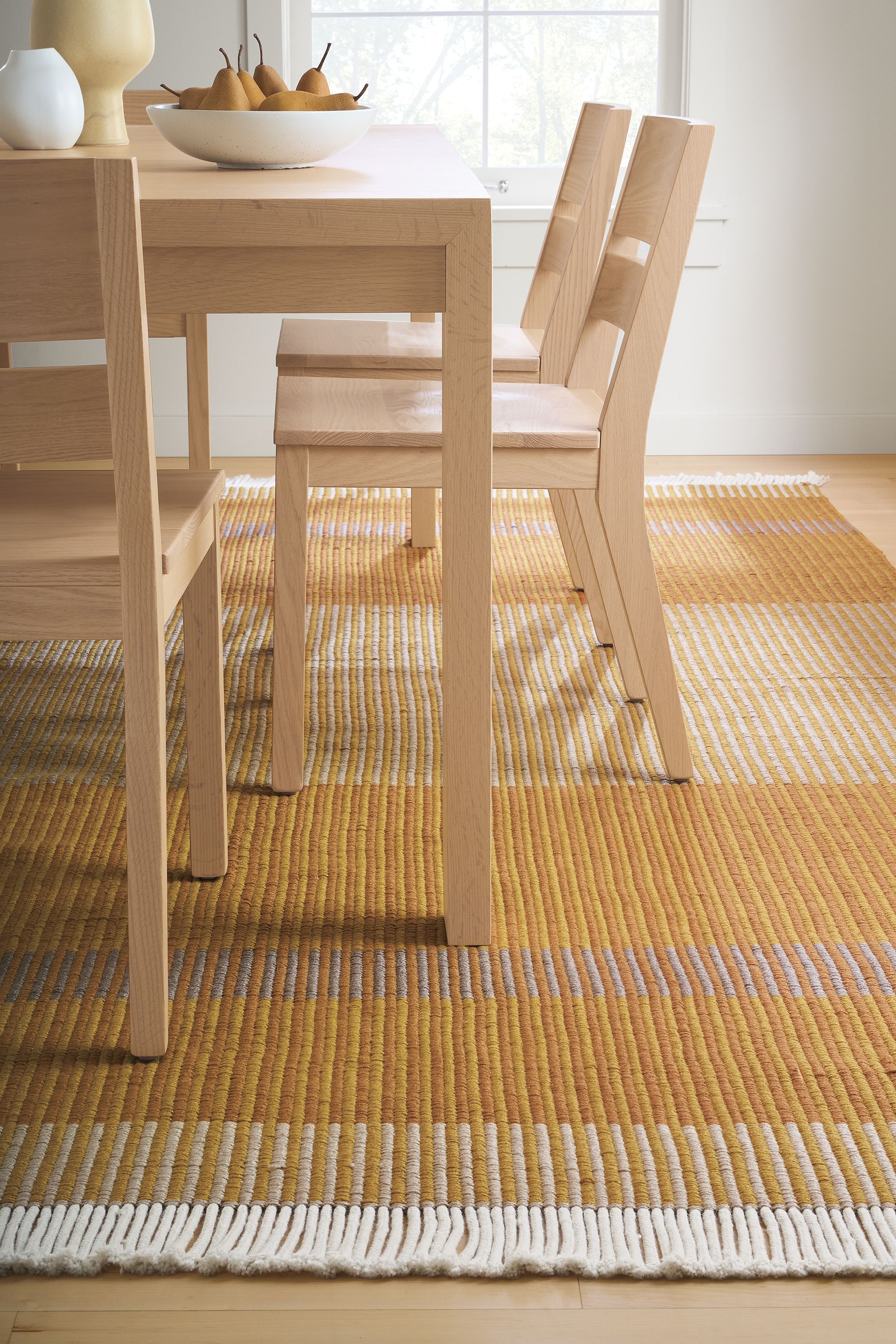 Dining room with detail of Ayla 8 by 10 rug in mustard and Walsh extension table and Afton side chairs in salt on red oak.
