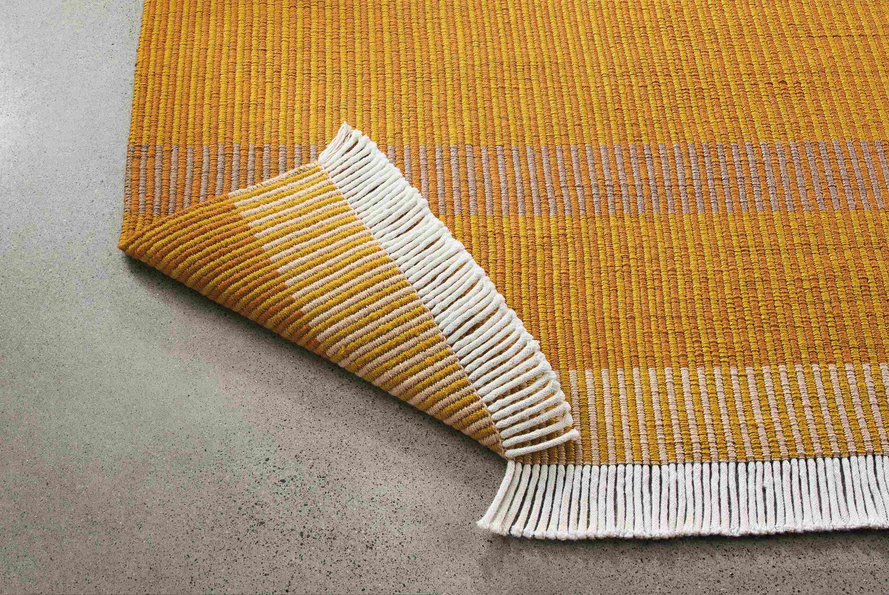 Detail of ayla 8 by 10 rug in mustard with corner turned up to show underside of rug.