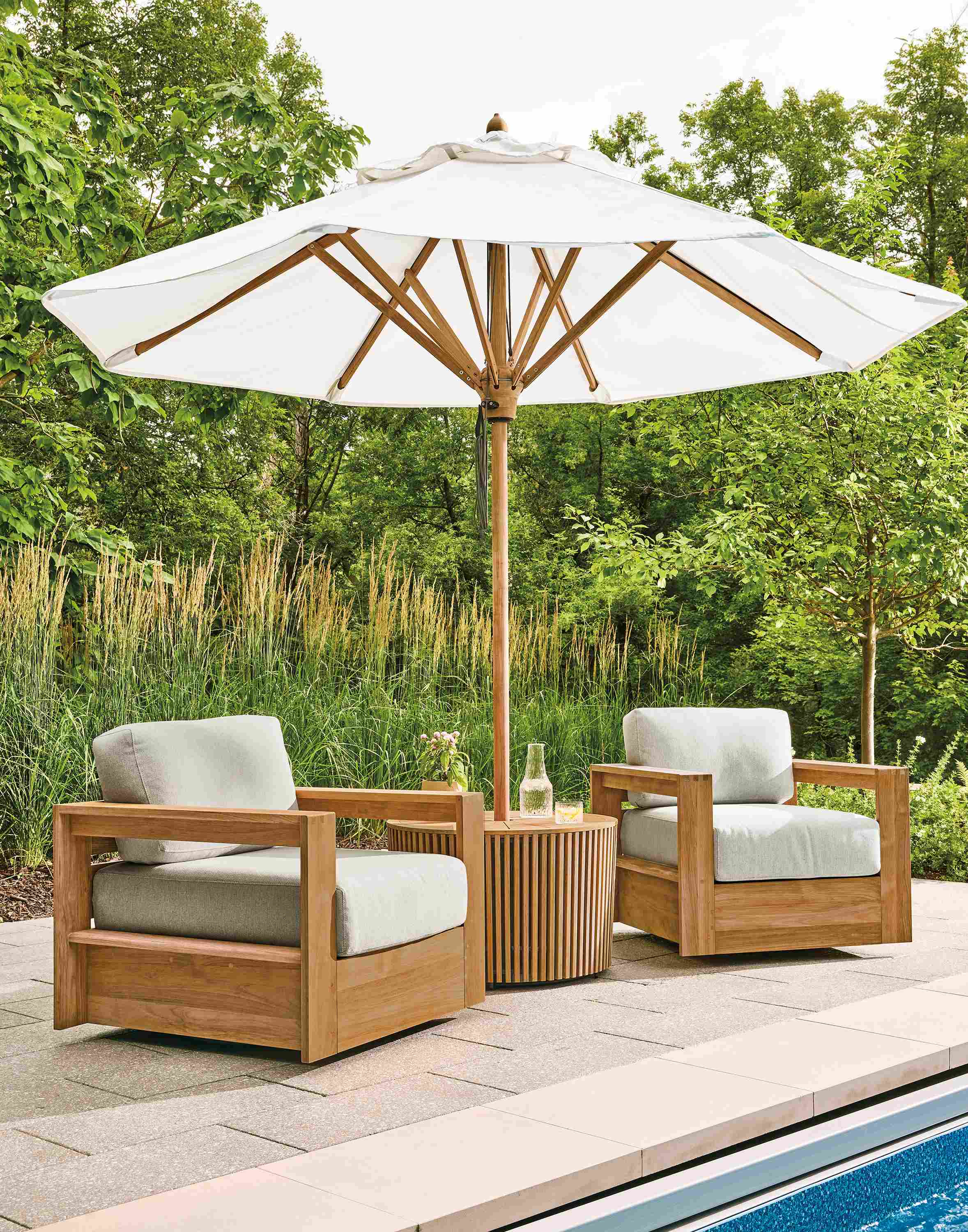 Poolside area with Banda 10-foot round patio umbrella with side table in teak heartwood and halo white fabric.
