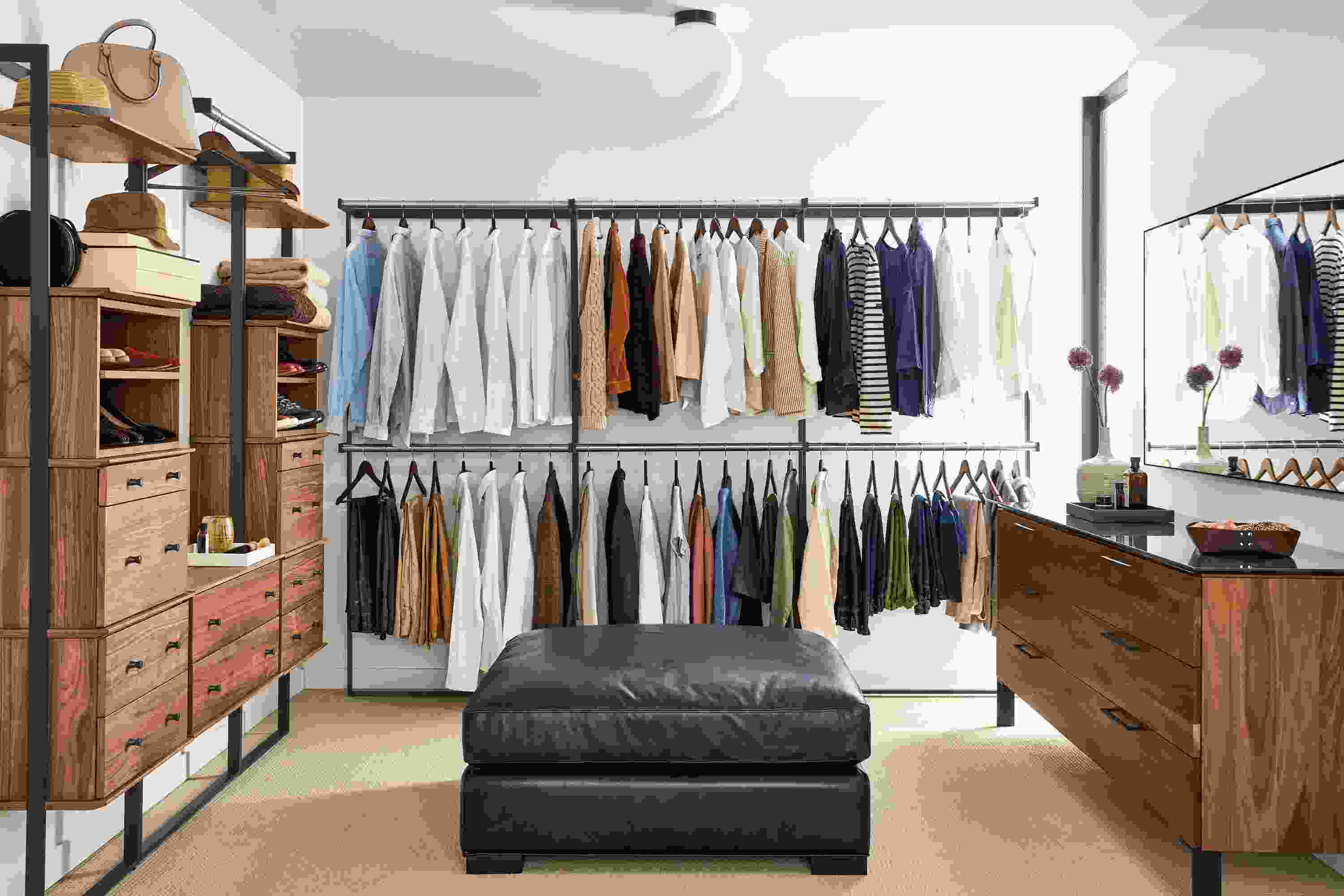 Large closet with multiple Beam bookcases with inserts and hanging closet racks in walnut and graphite, Kenwood dresser in walnut and metro ottoman.