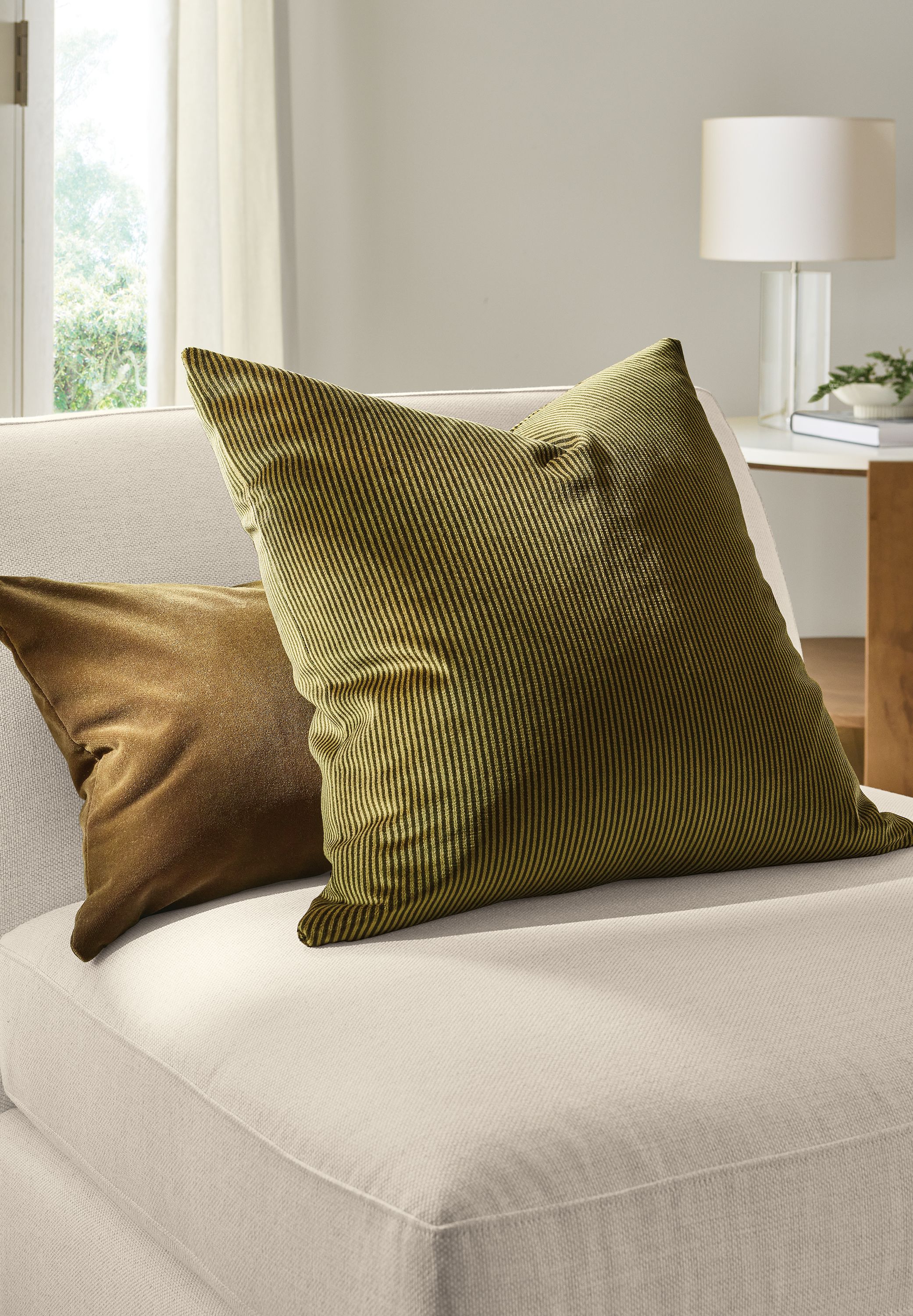Detail of a Beller 20 by 20 throw pillow in olive and Redding Velvet pillow in bronze on an Astaire chair in Sumner Ivory.