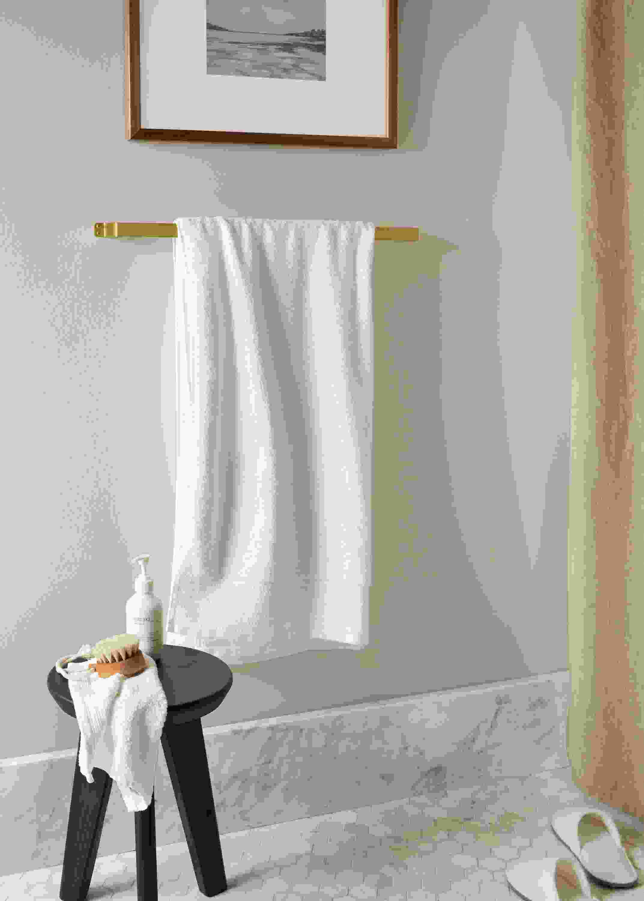 Bend towel rack in gold holding Fendwick towel in white in a bathroom.