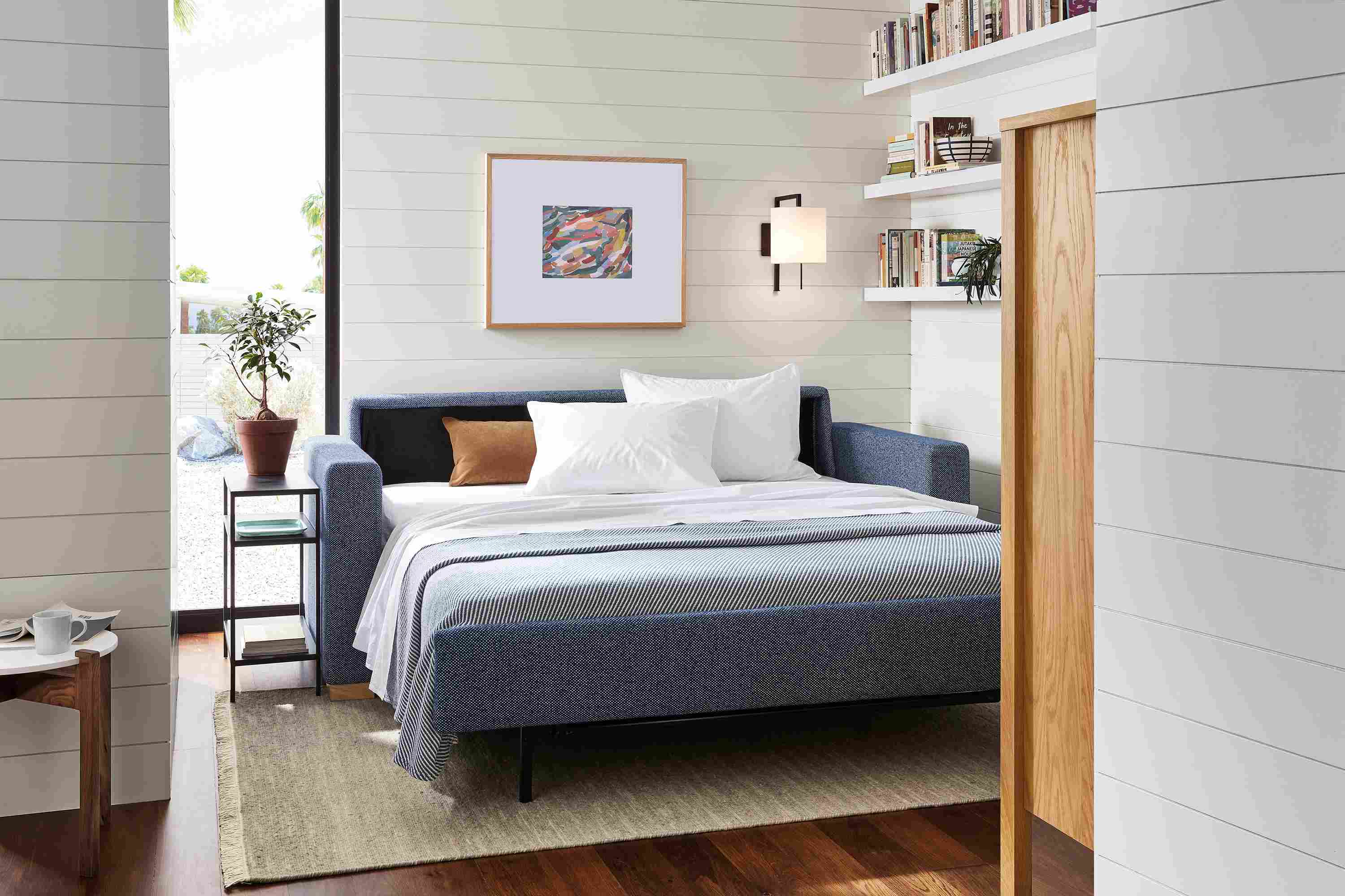 Small living space with Berin 82-wide sleeper sofa in Arin Navy in open position with slim end table.