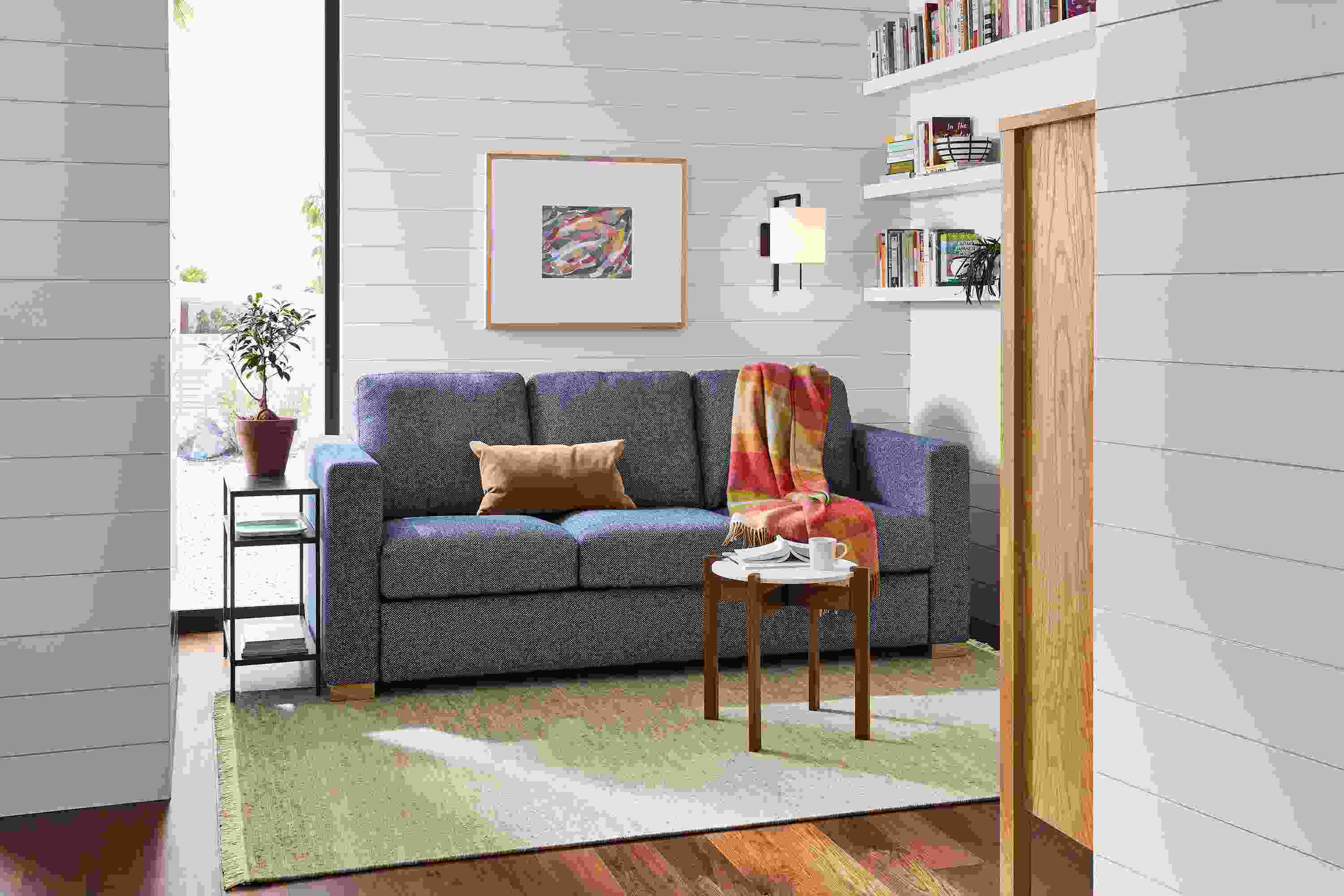 Small living space with Berin 82-wide sleeper sofa in Arin Navy, Kavala End Table in Walnut and White and Slim table in Natural Steel.