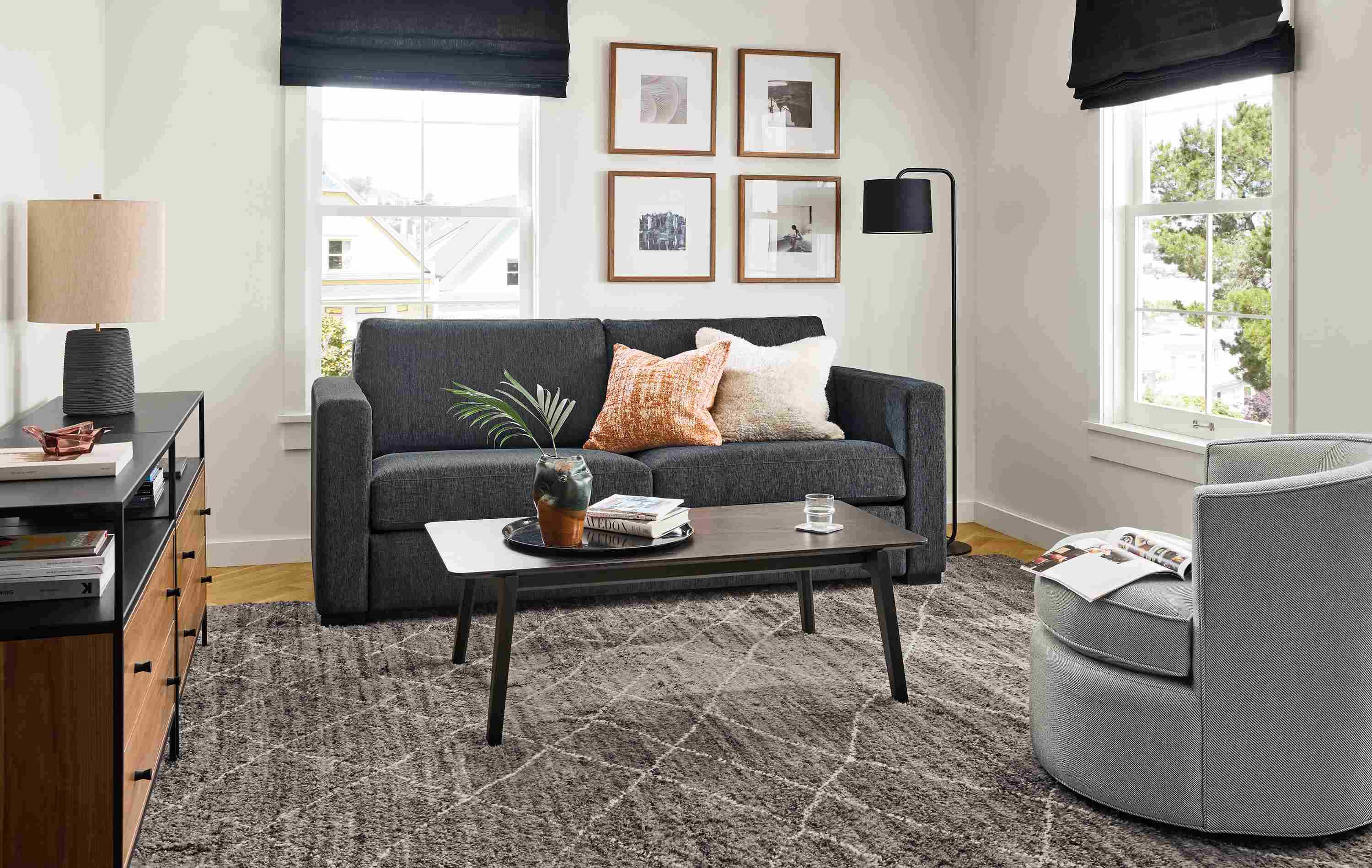 Living room with Berin 82-wide queen-plus sleeper sofa in crawford navy, Otis swivel chair in Derry Cement and Orlin table.