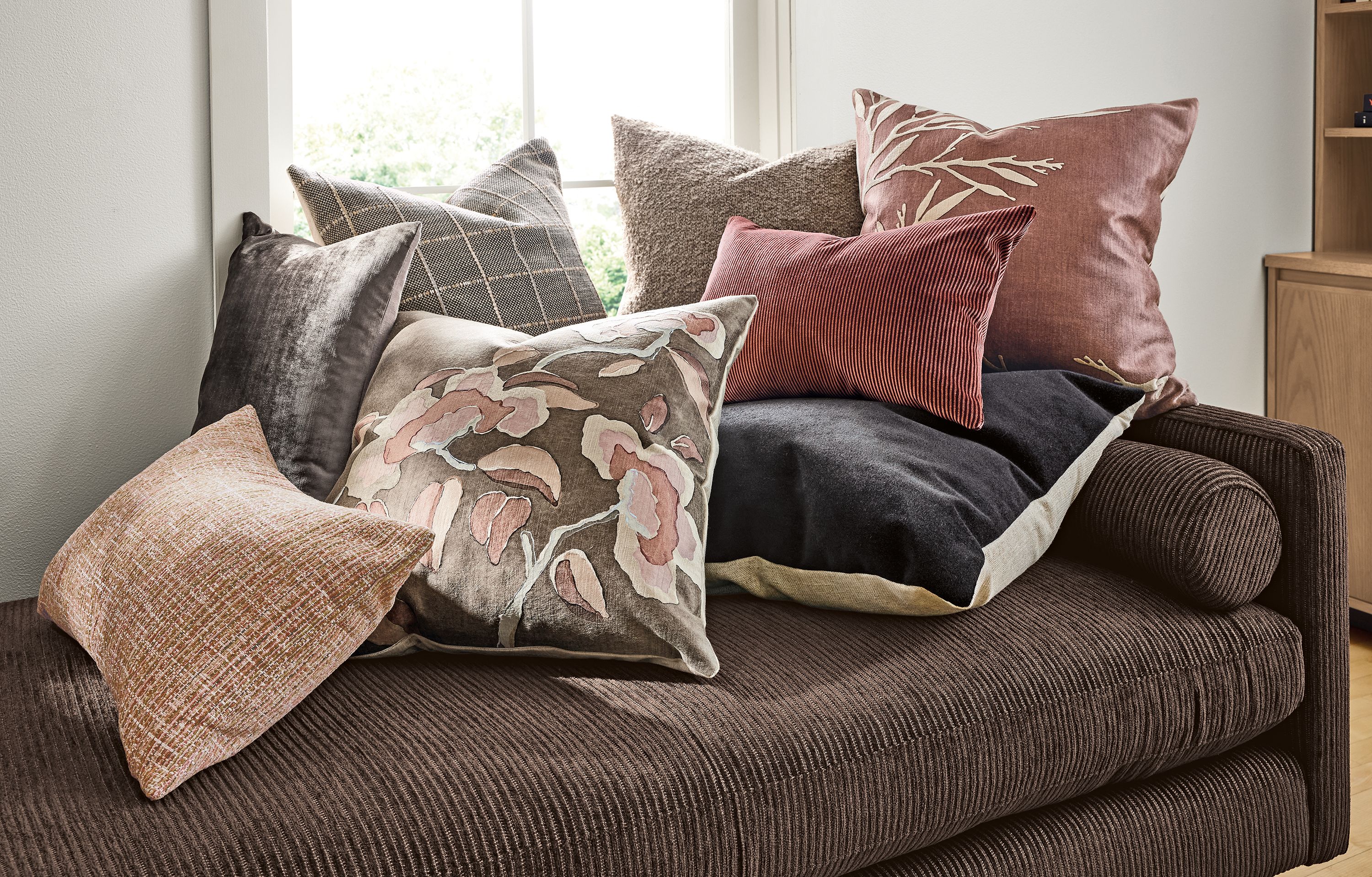 A group of pillows including Besson, Sandon, Blossom, Beller, Liana on a Jasper sofa in Brava Umber.