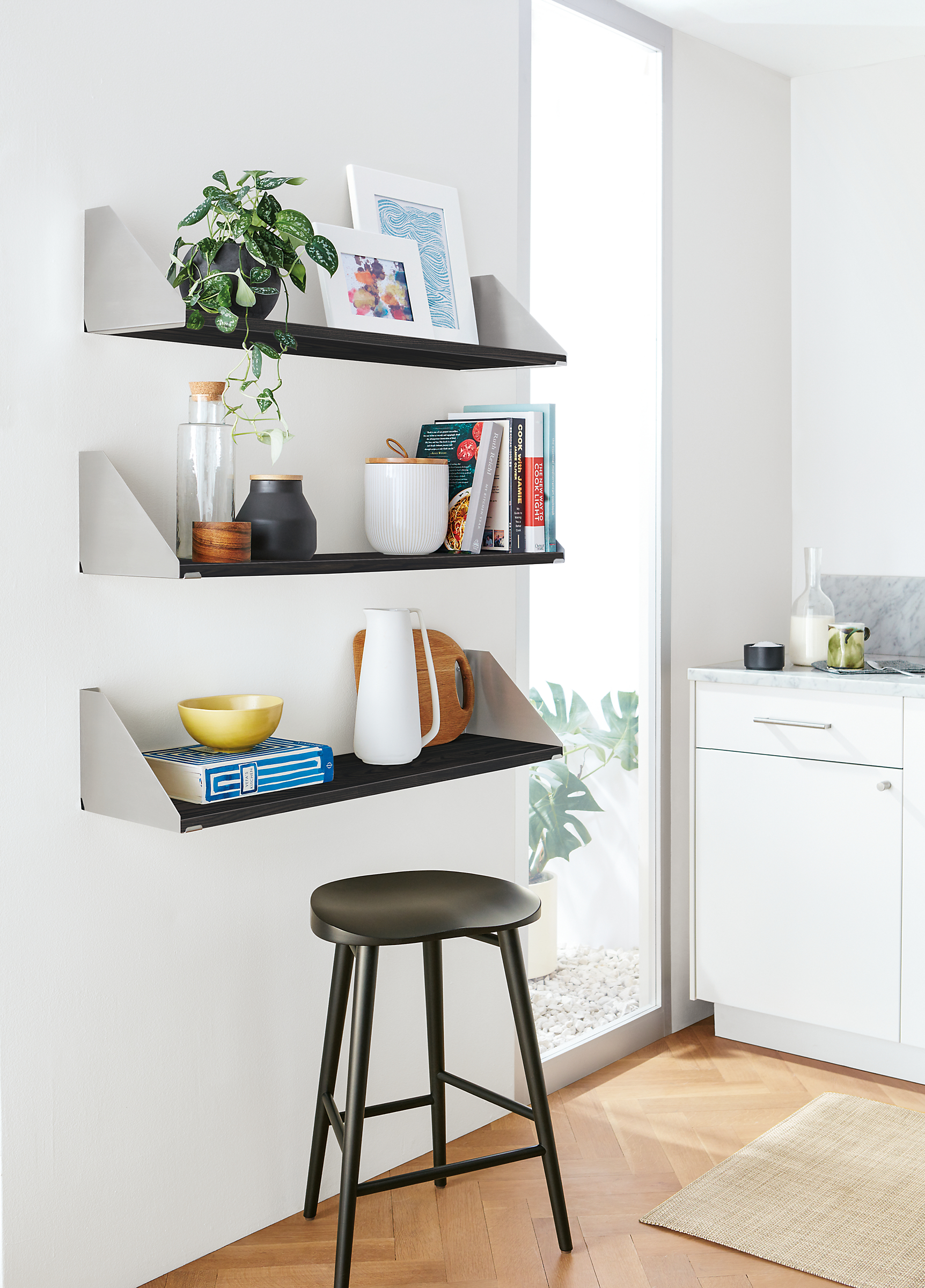 three bradley wall shelves in stainless steel holding frames, books and kitchen objects.