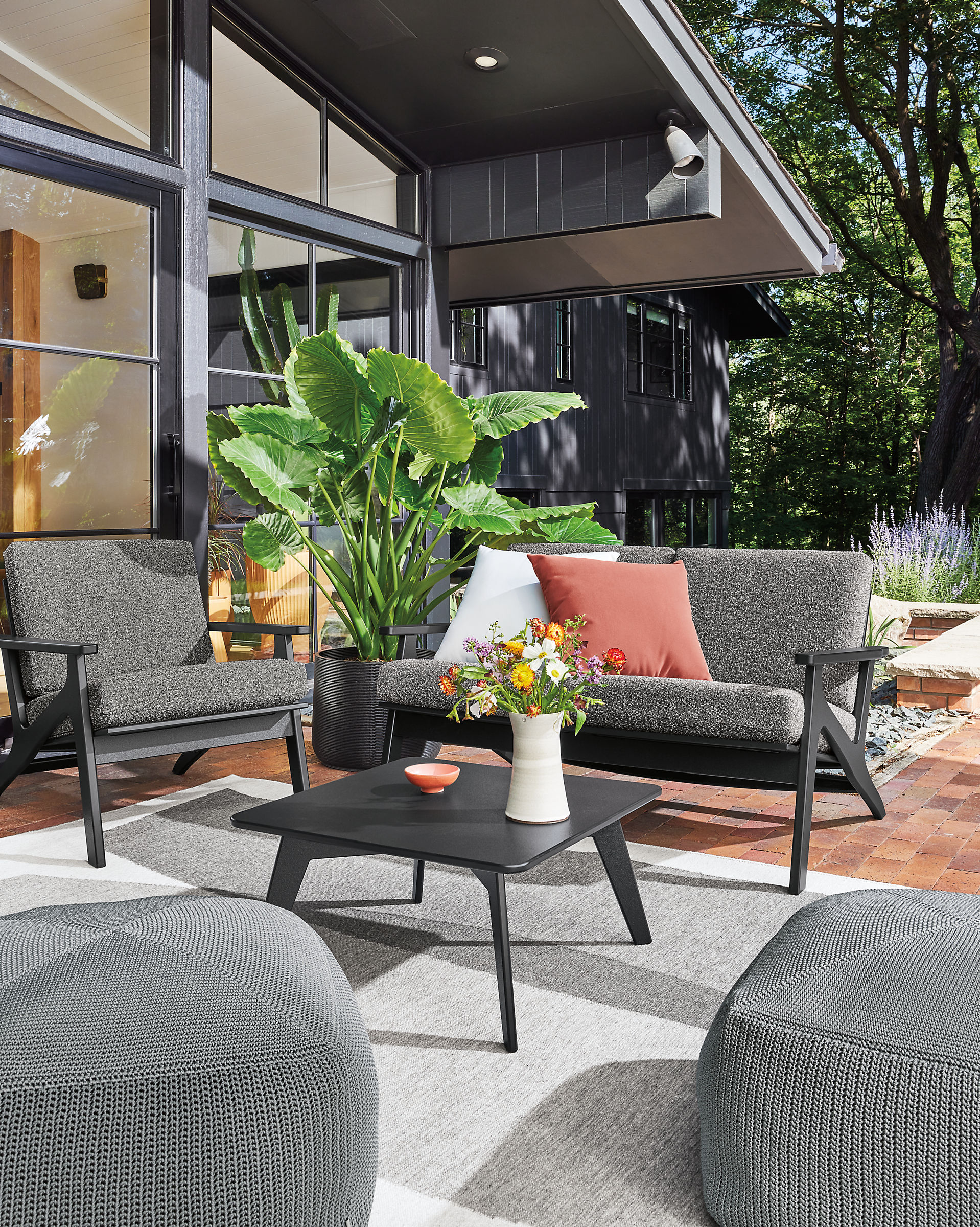 Breeze outdoor sofa and chair in black with kloss charcoal cushions, nova table and zena poufs in grey.