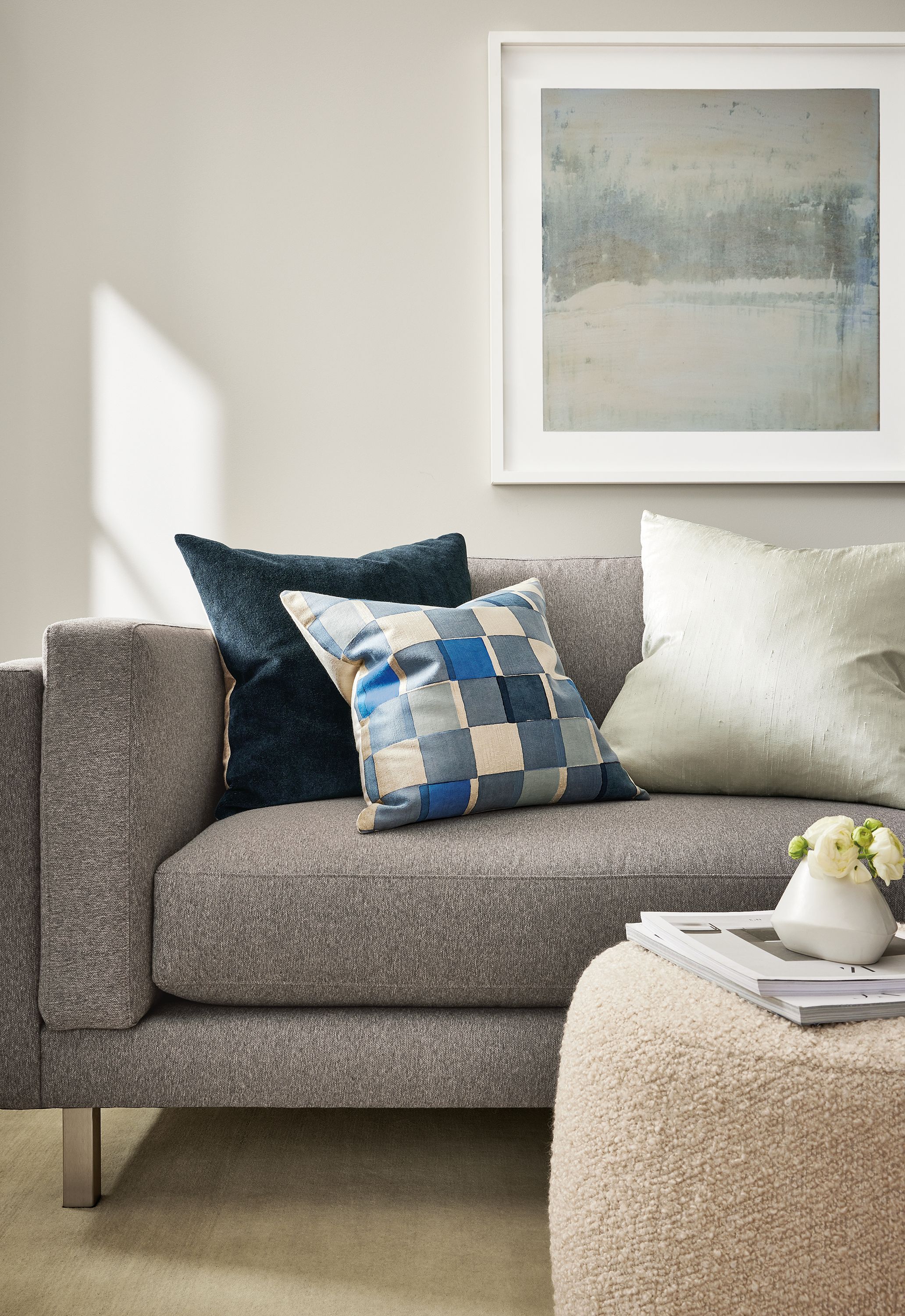 Living room with Cade sofa in Flint Grey, Lind 42-diameter ottoman in Dornick Ivory and various throw pillows.