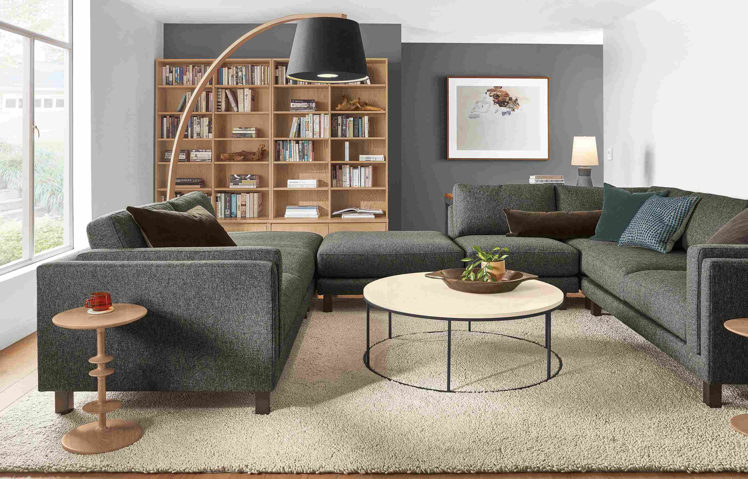 Living room with cade 6-piece sectional in tepic charcoal and tyne round coffee table in  natural steel with ecru quartz top.