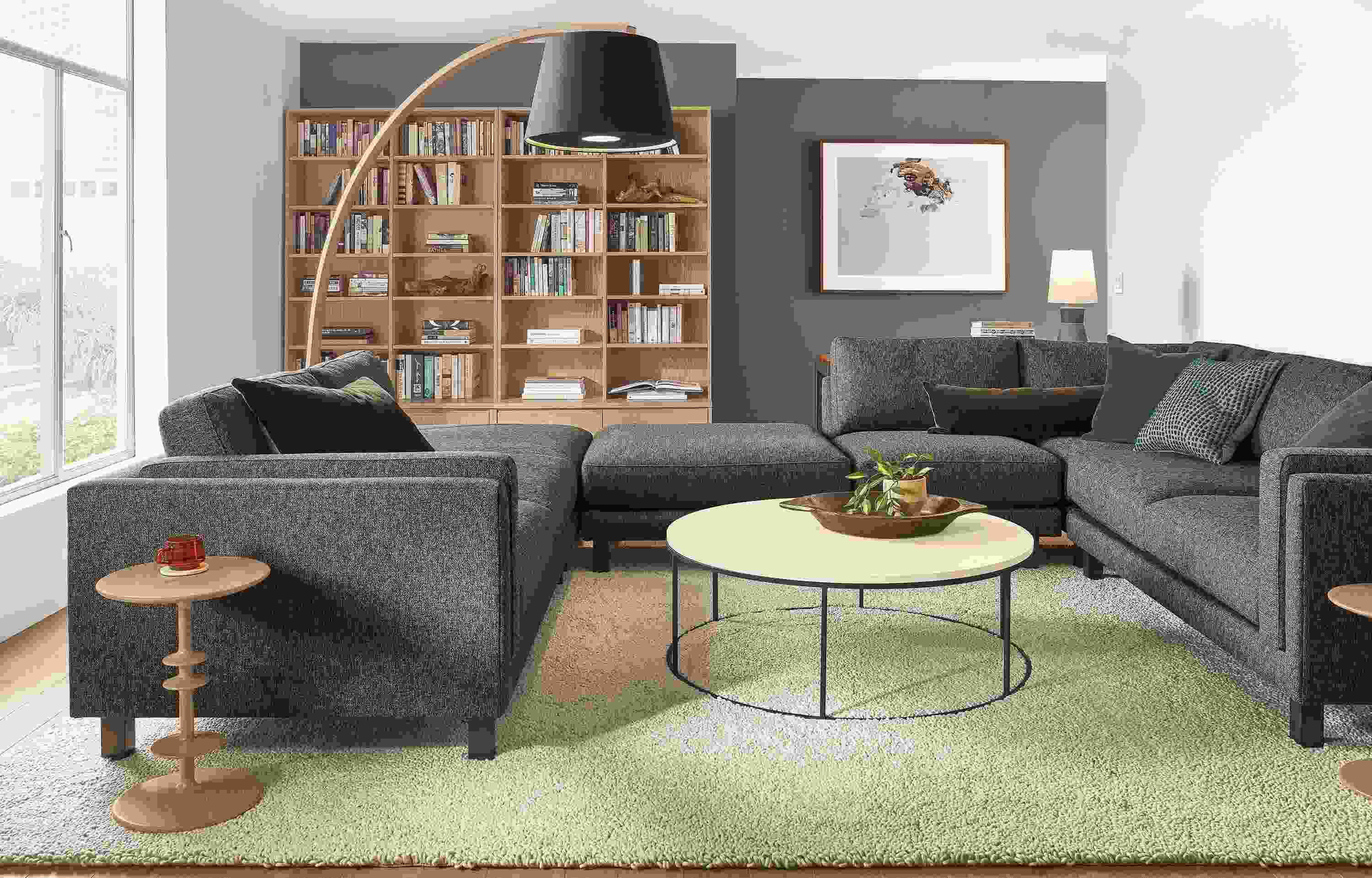 Living room with cade 6-piece sectional in tepic charcoal and tyne round coffee table in  natural steel with ecru quartz top.