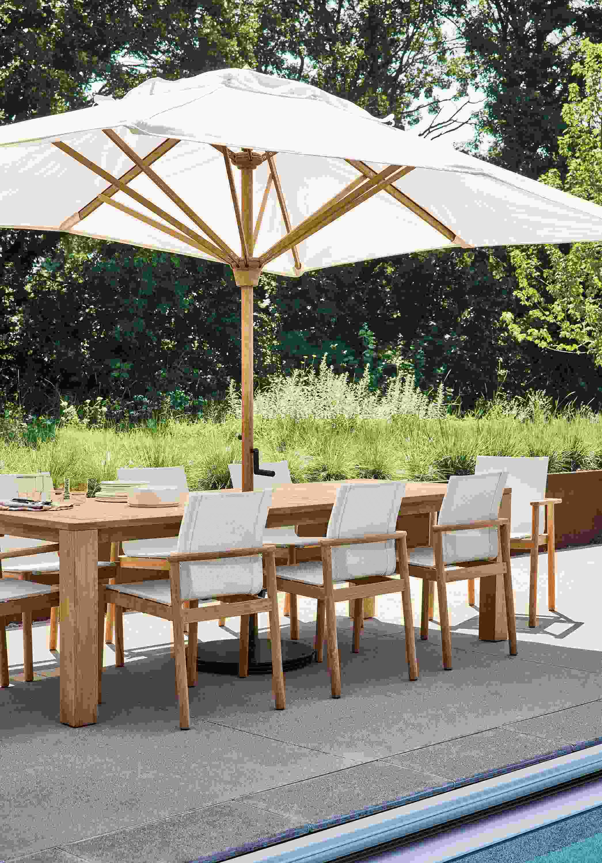 Poolside area with Capri 97-wide table in teak heartwood and Peri chairs in teak heartwood.