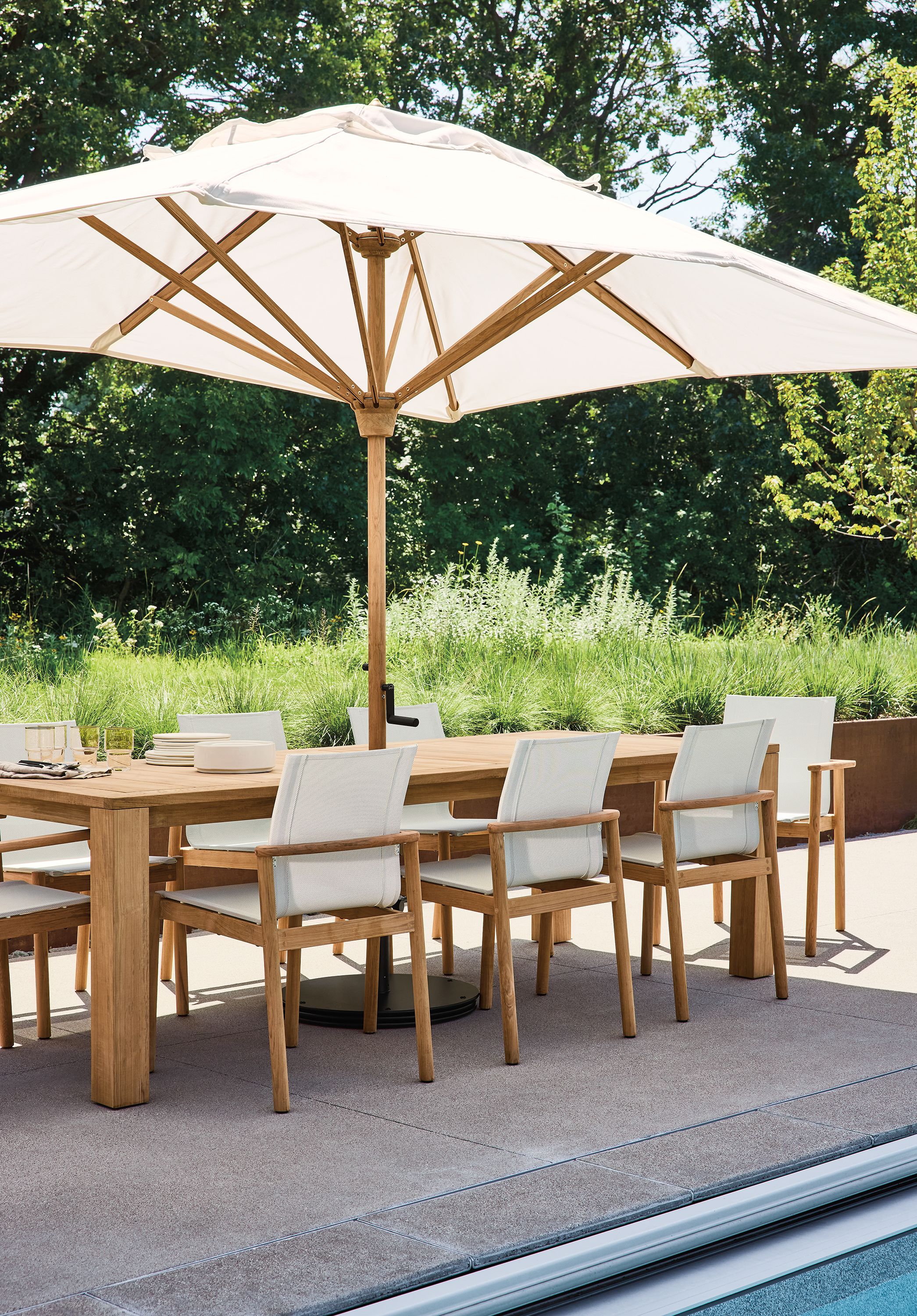 Poolside area with Capri 97-wide table in teak heartwood and Peri chairs in teak heartwood.