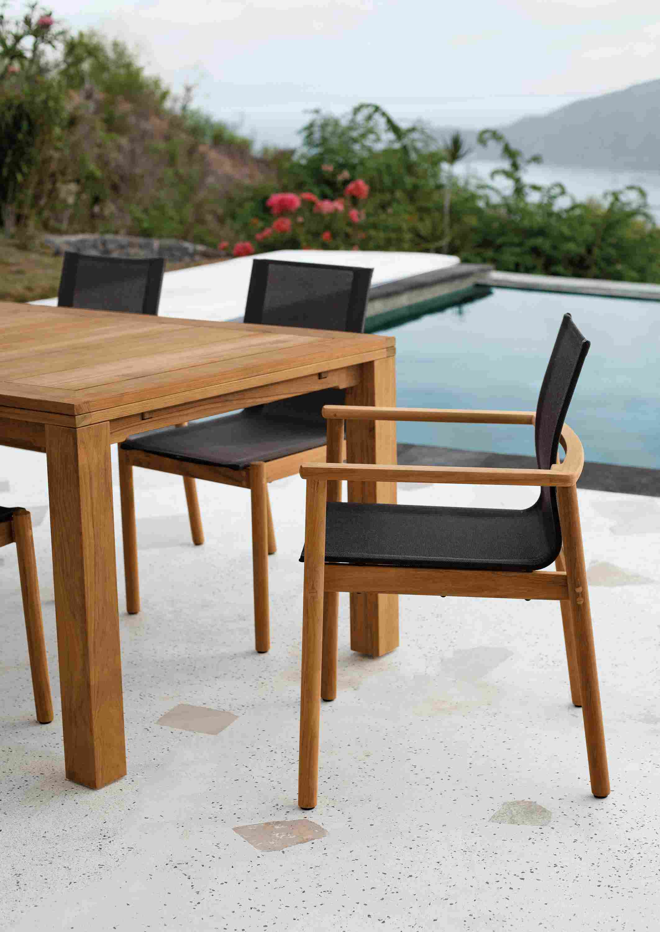 Side view of Peri Arm Chair in teak with Slate Sling and Capri outdoor table in teak.
