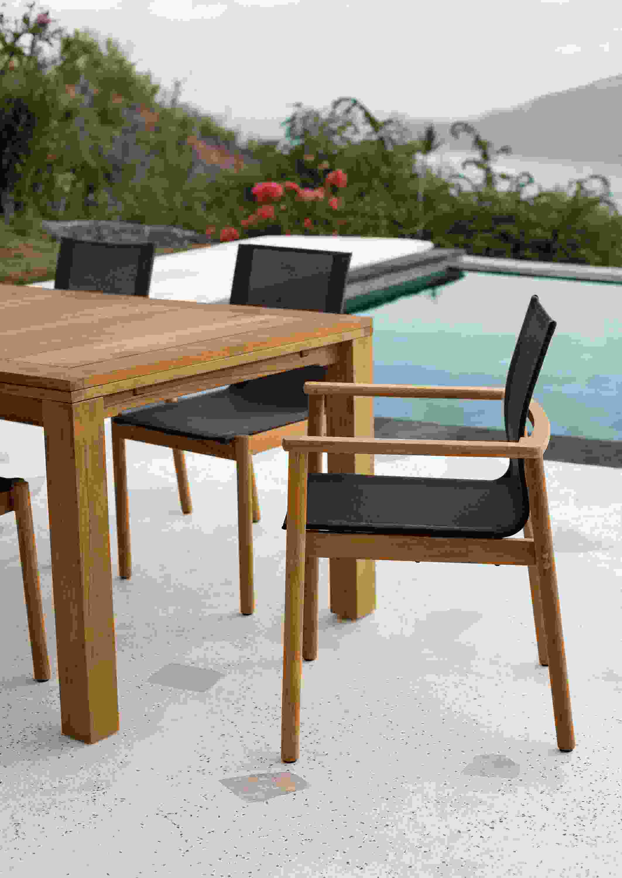 Side view of Peri Arm Chair in teak with Slate Sling and Capri outdoor table in teak.