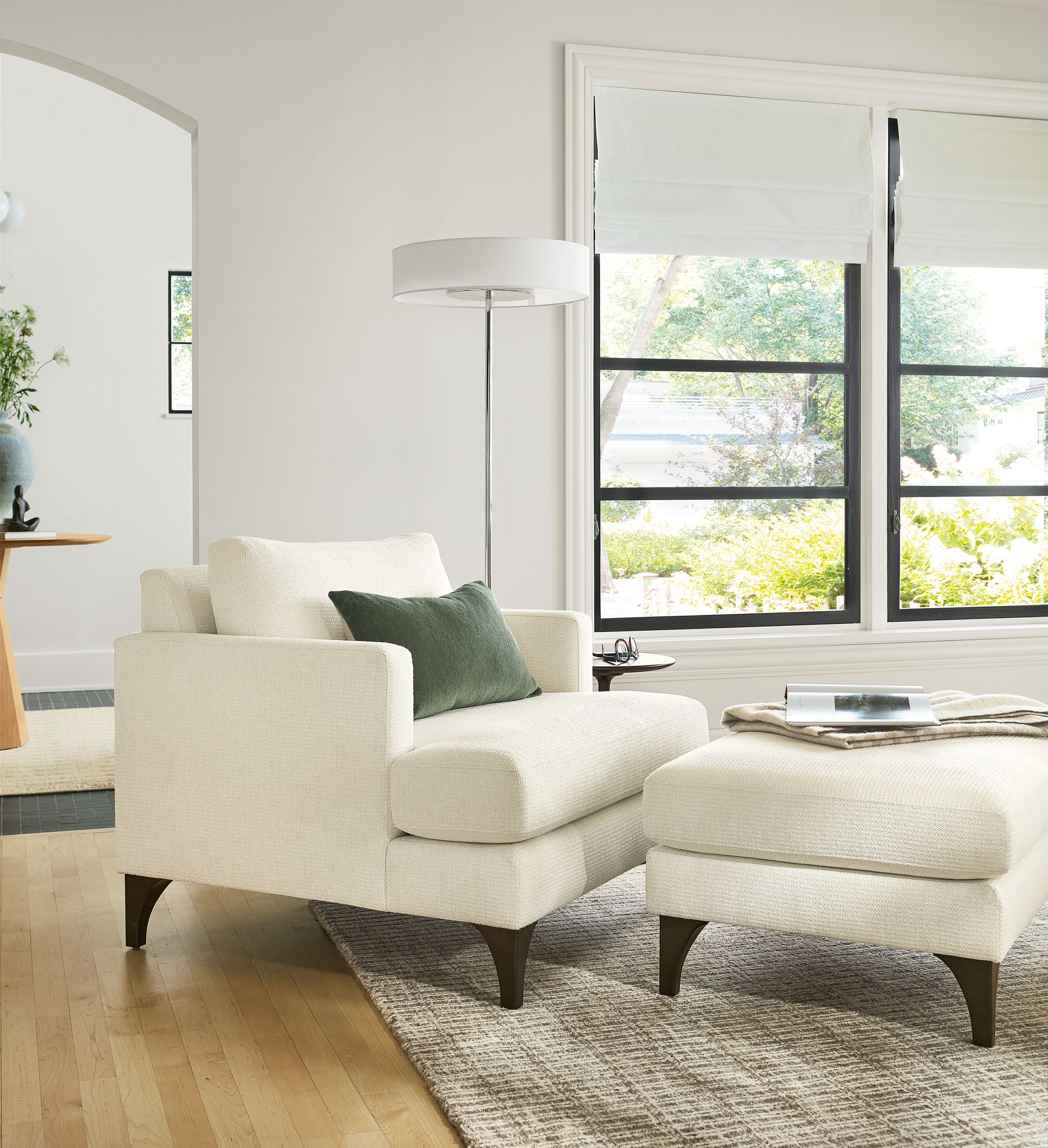 Living room with Carlton chair and ottoman in Orla White, Cohen floor lamp in polished nickel and Nera 8 by 10 rug in stone.