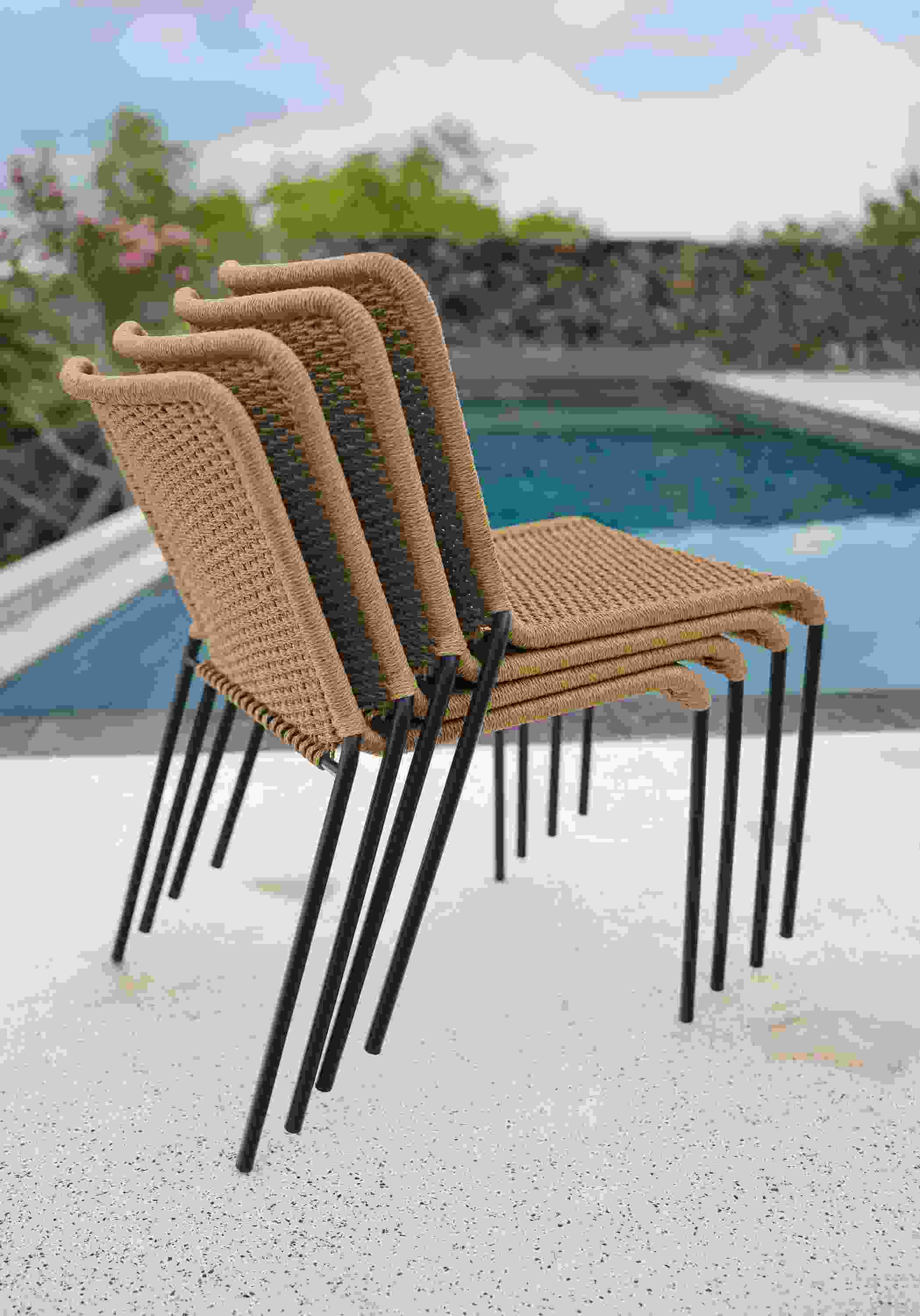 Stack of four Clea Outdoor Side Chairs in Natural cording with black legs.