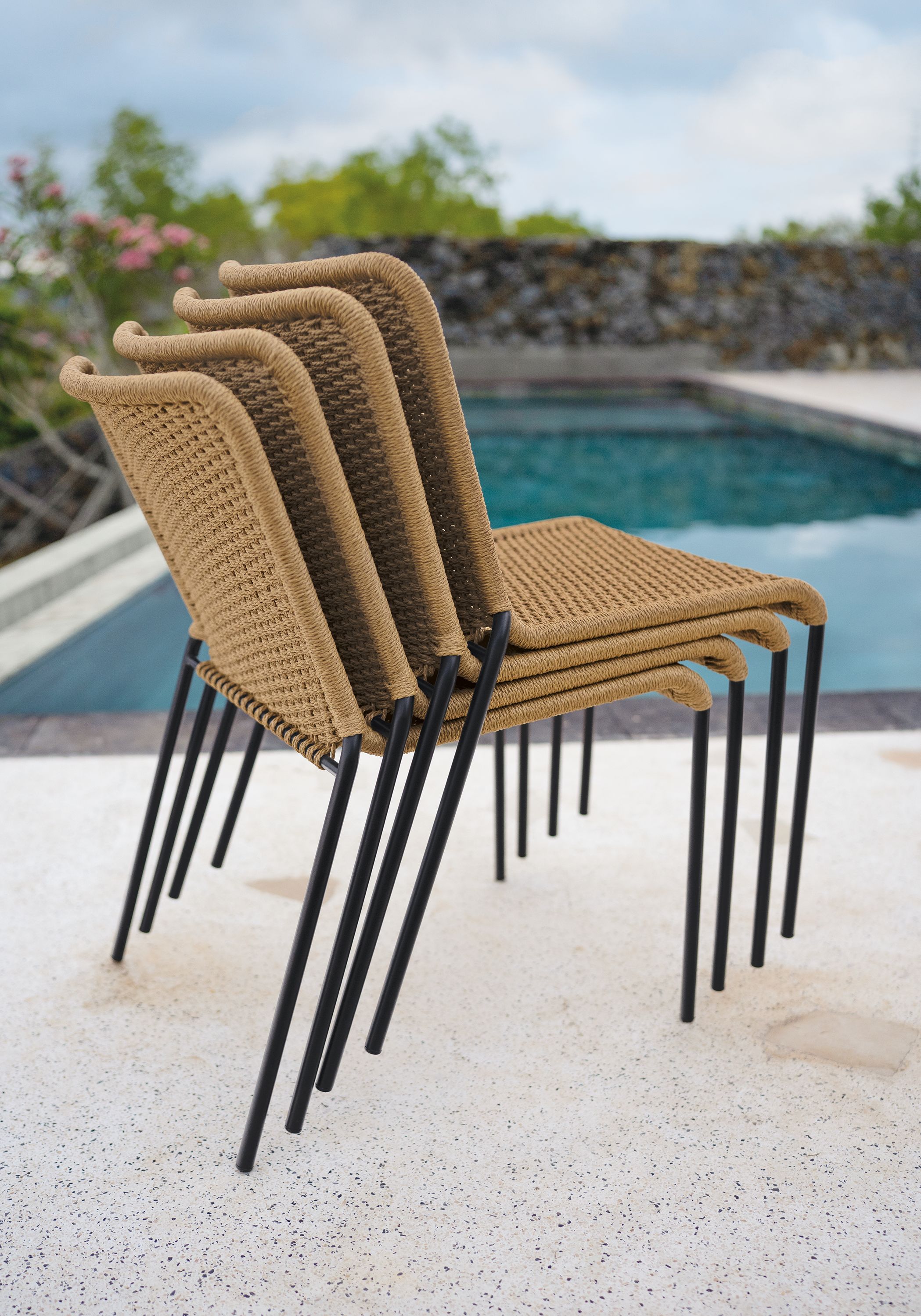 Stack of four Clea Outdoor Side Chairs in Natural cording with black legs.
