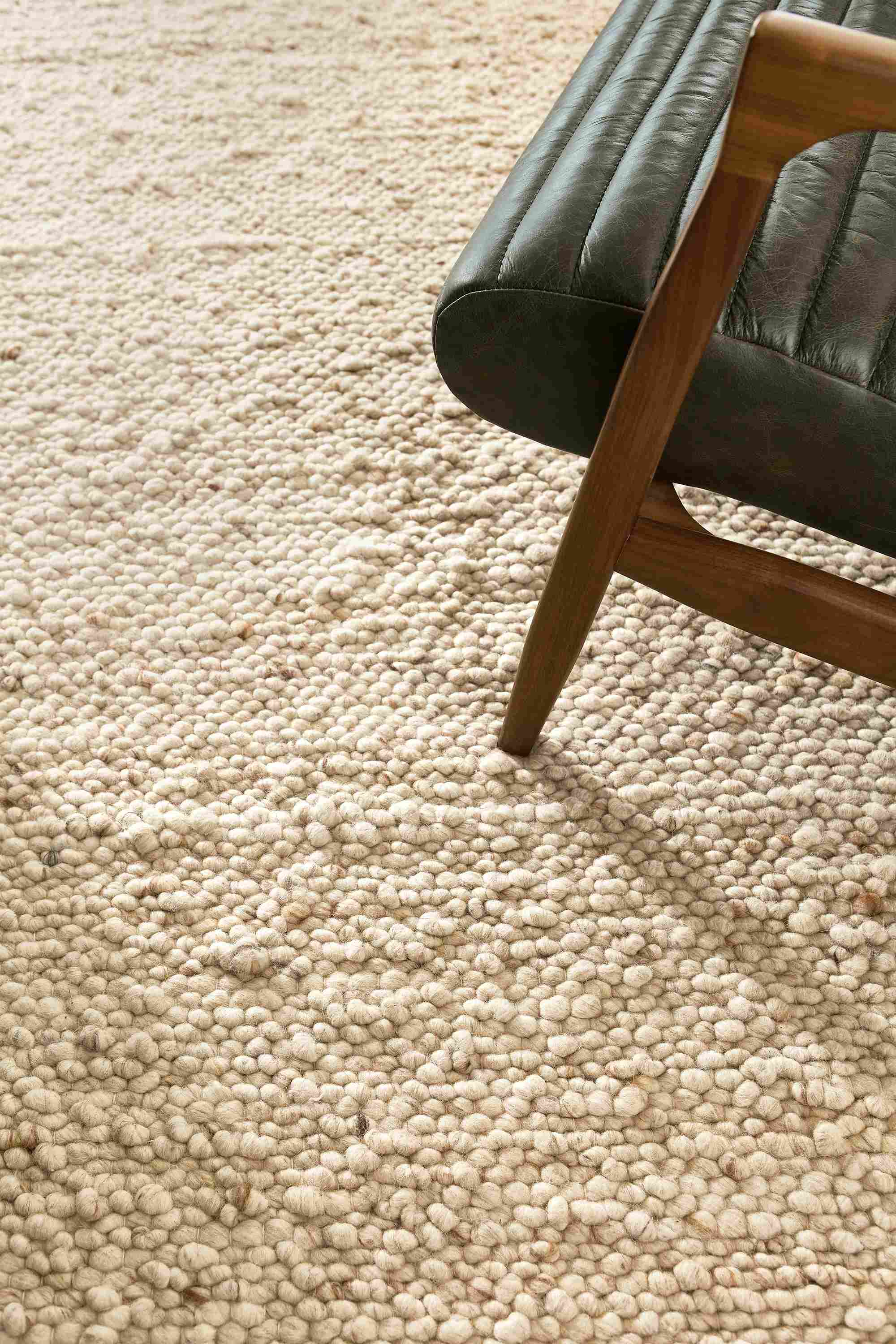 Detail of cobble 8 by 10 rug in ecru and callan chair in palermo olive with walnut legs.